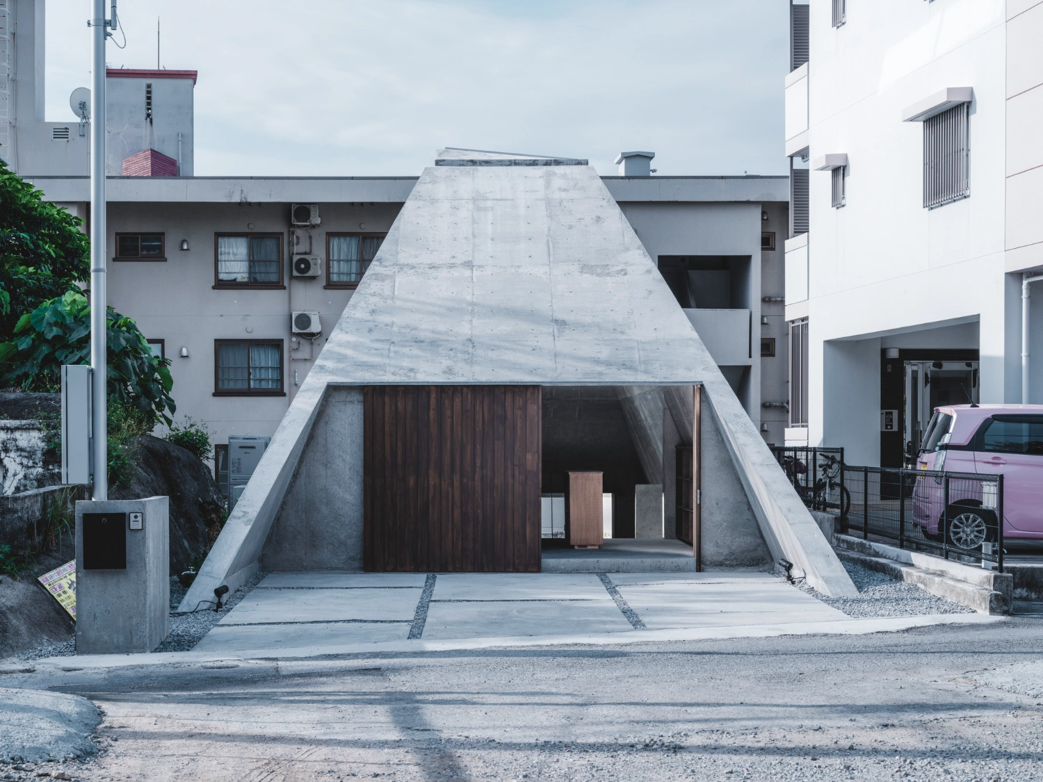 Pyramid Hut by IGArchitects — Pyramid Hut's trapezoidal concrete facade dominates the forecourt, its monolithic form defined by visible board-formed seams and weathered surface texture.