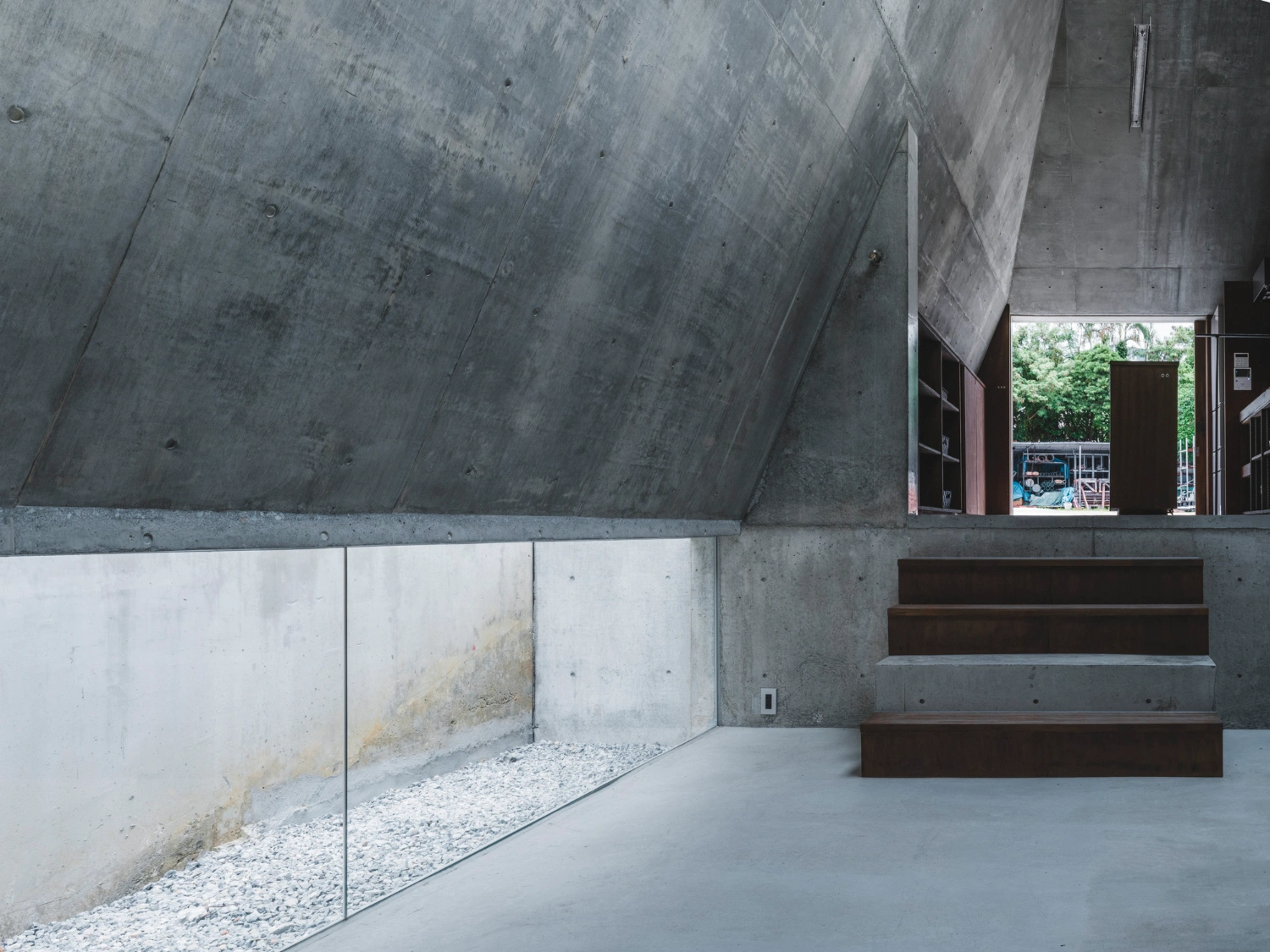 Pyramid Hut by IGArchitects — A sunken forecourt framed by a monolithic concrete pyramid form, its board-formed surface displaying seams and weathering marks.