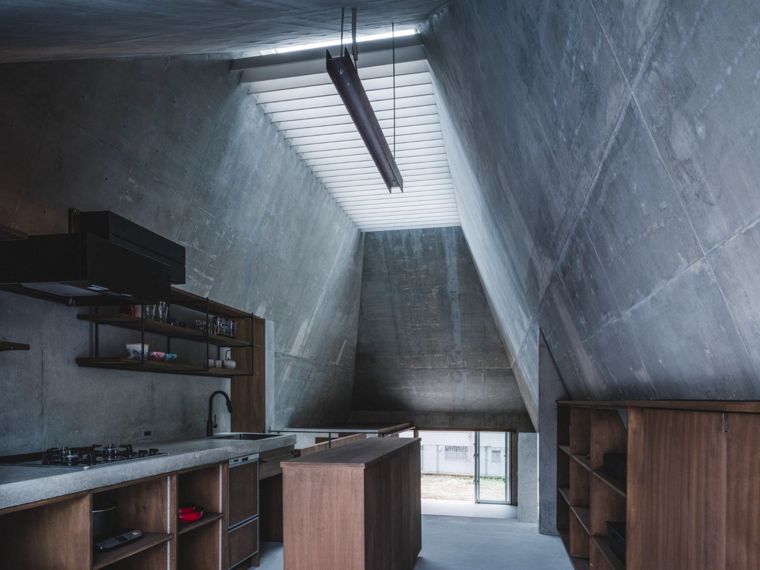 Pyramid Hut by IGArchitects — The kitchen interior reveals the project's material honesty through board-formed concrete walls and ceiling, marked by distinct formwork seams and...