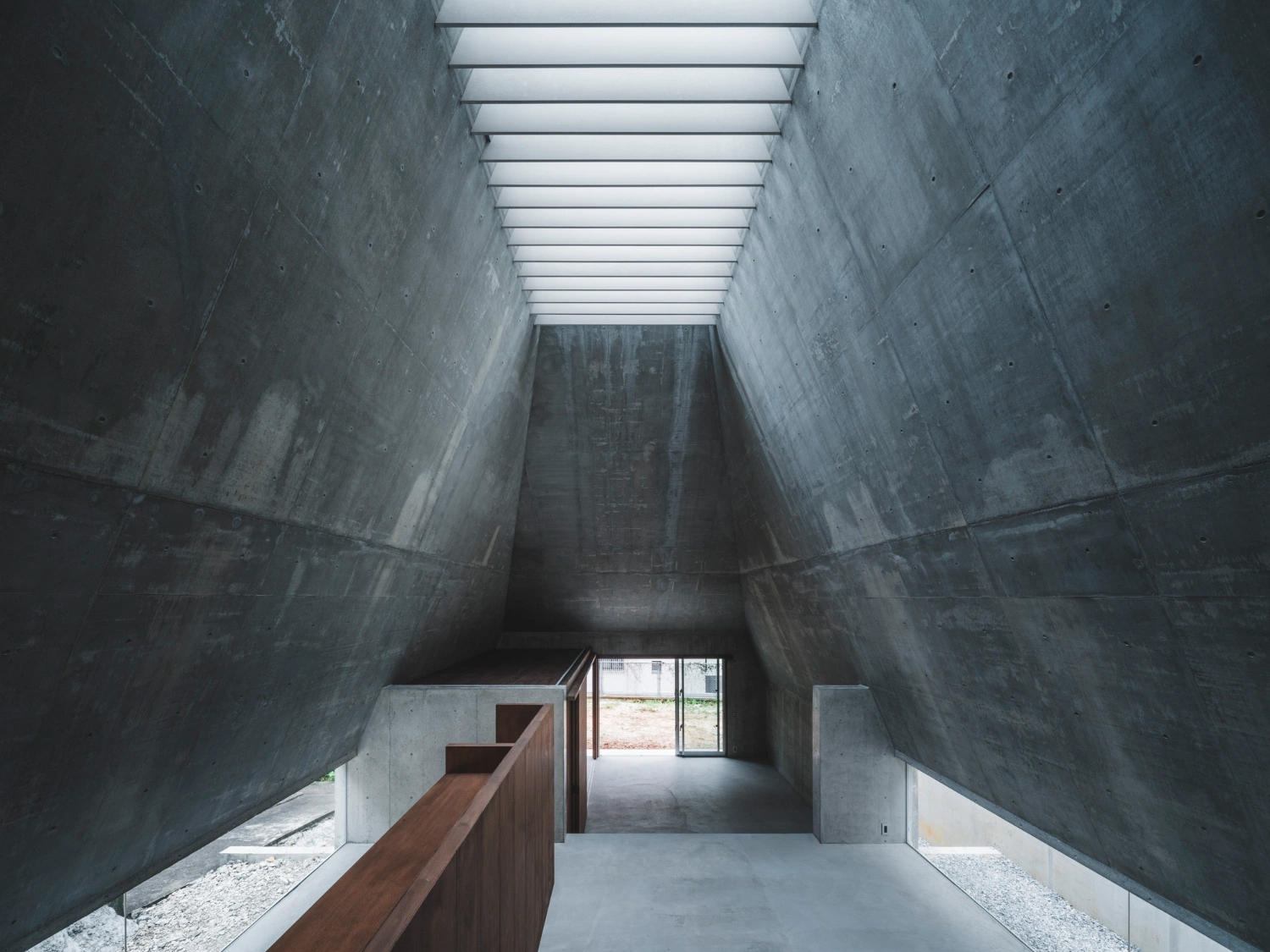 Pyramid Hut by IGArchitects — A deep interior passage framed by monolithic concrete walls rises toward a linear skylight running the full length of the ceiling.