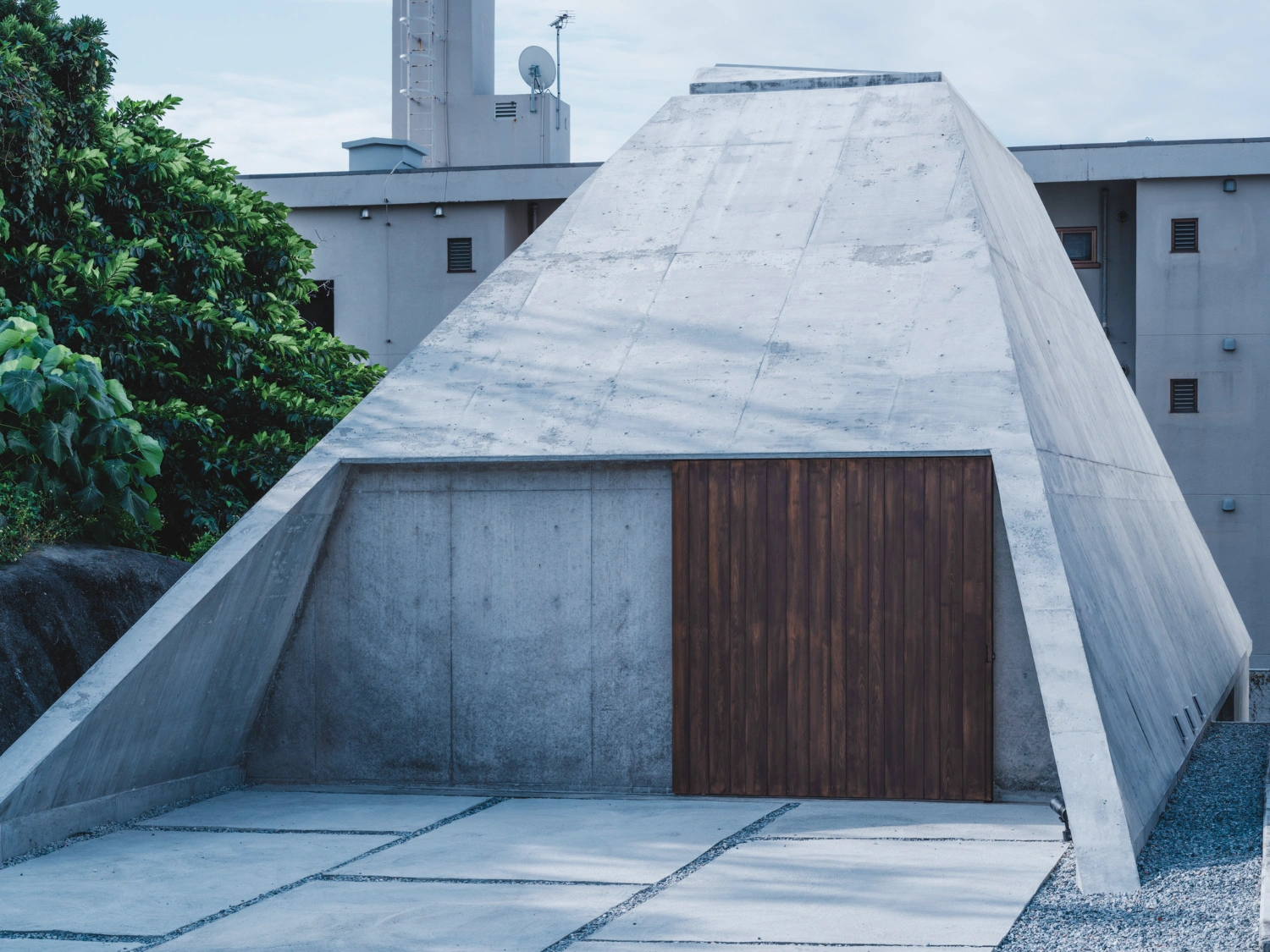 Pyramid Hut by IGArchitects — The pyramid-form residence presents its monolithic concrete mass to the forecourt, where a trapezoidal facade reveals board-formed concrete with visible...