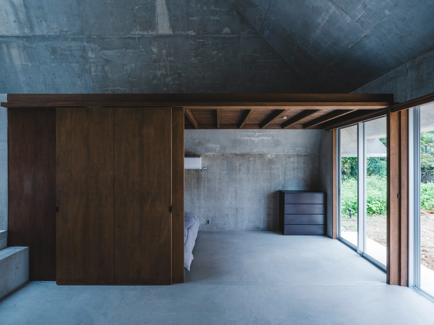 Pyramid Hut by IGArchitects — Interior view revealing the spatial relationship between the dark timber-clad wardrobe system and the concrete structural frame.