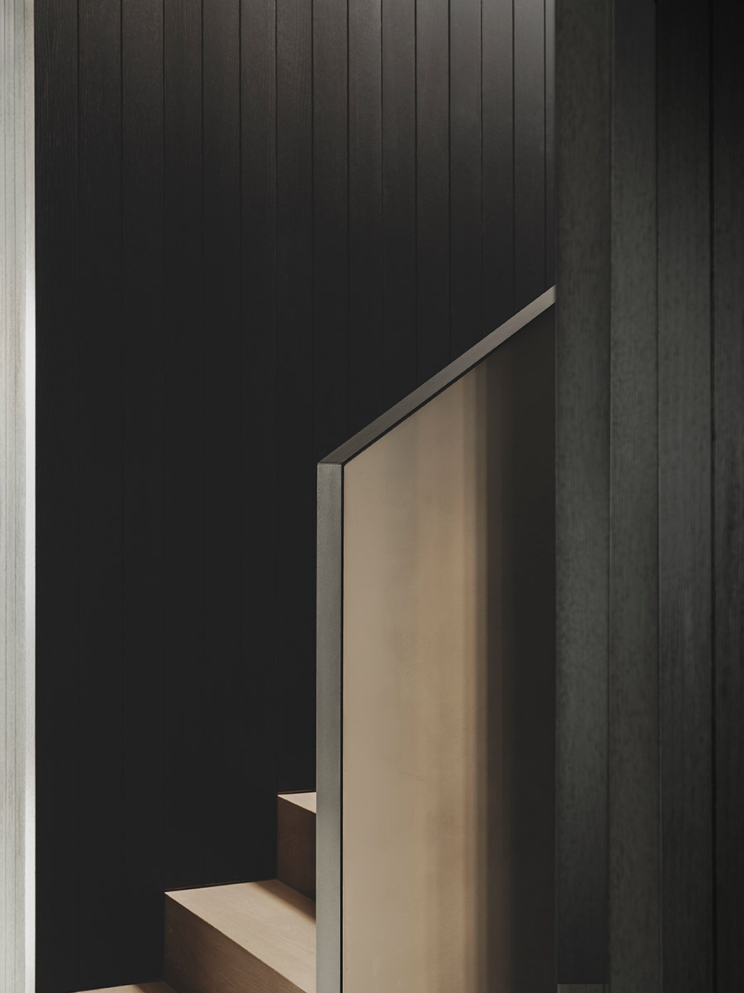 S29 House by Francesc Rifé Studio + Exit Projectes — A recessed niche carved into vertically board-formed dark timber paneling reveals a light-filled passage beyond.