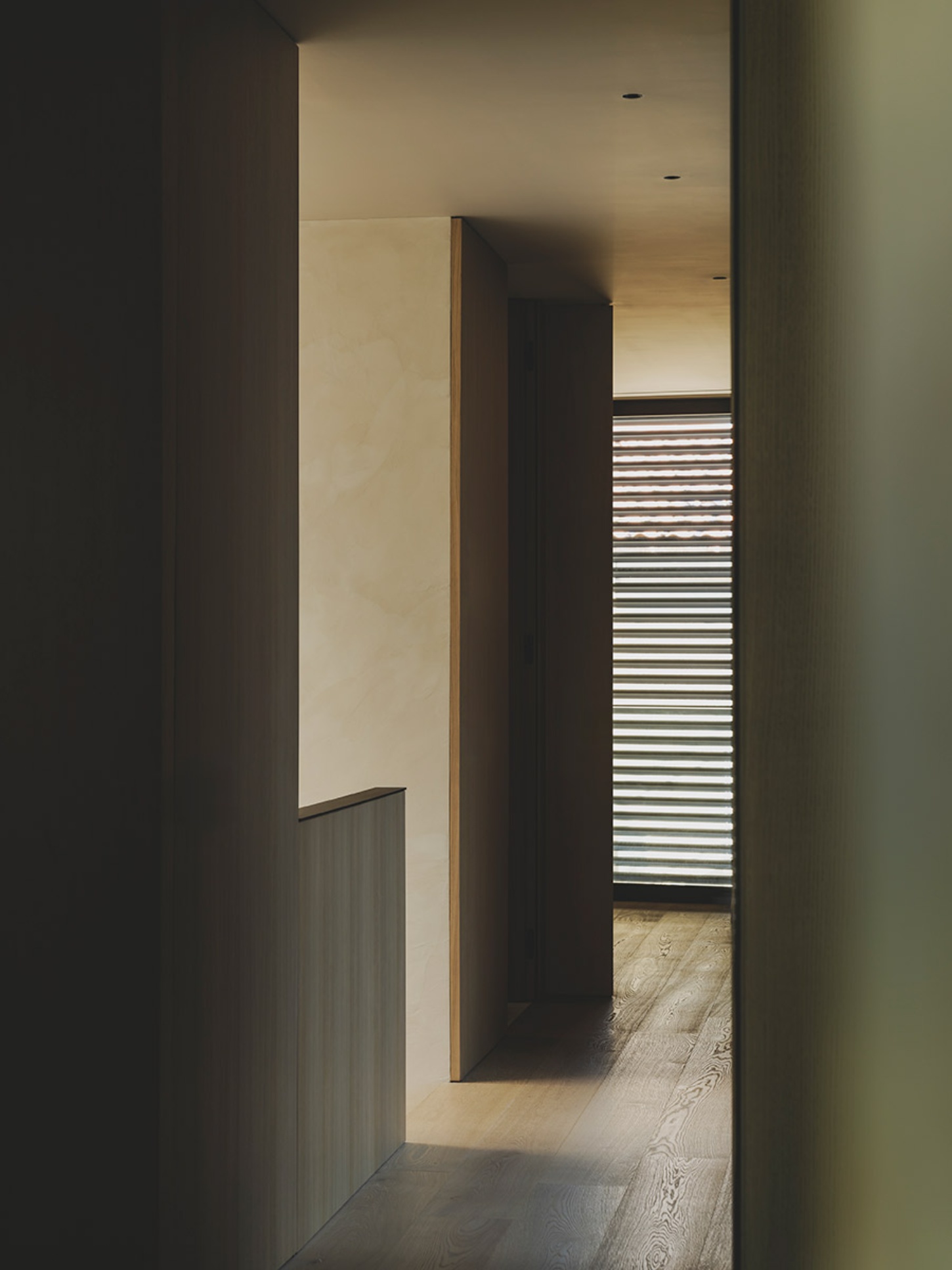 S29 House by Francesc Rifé Studio + Exit Projectes — A corridor passage frames layered spatial depth, with cream-painted plaster walls flanking a dark timber-clad central volume.