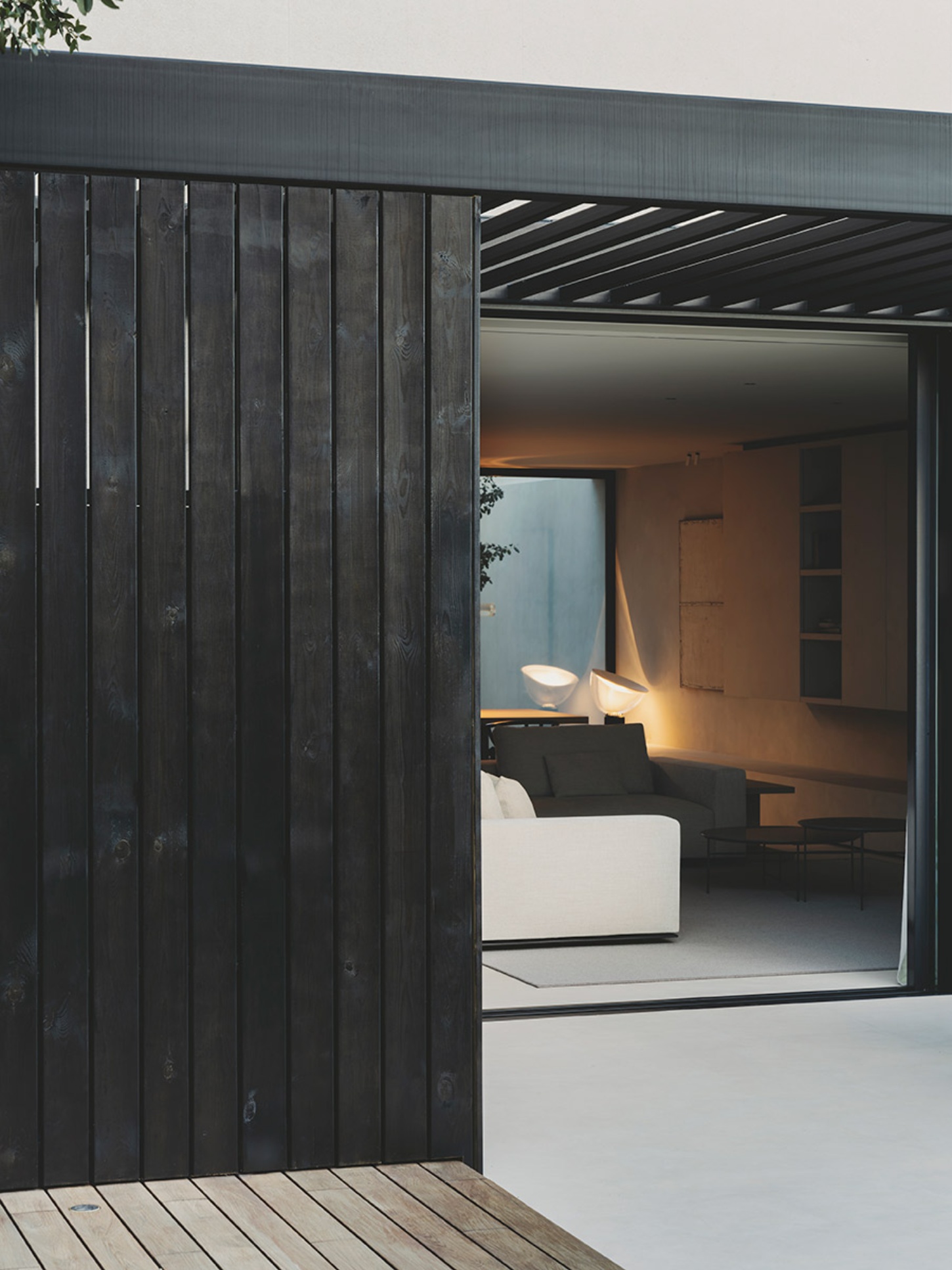 S29 House by Francesc Rifé Studio + Exit Projectes — The threshold between exterior and interior reveals a studied material contrast: weathered black-stained timber vertical slats frame a sliding glass...
