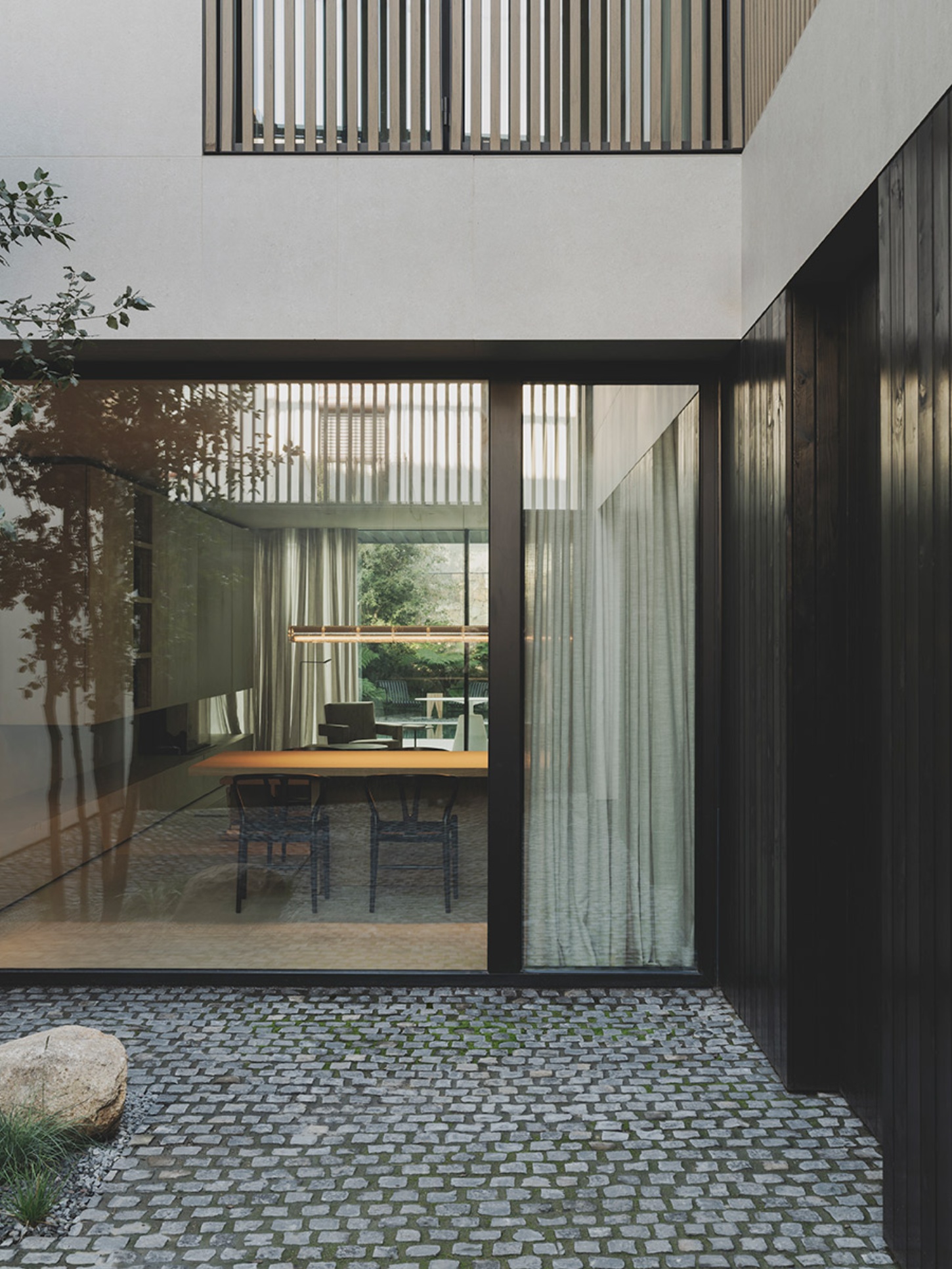 S29 House by Francesc Rifé Studio + Exit Projectes — The courtyard threshold frames a dining pavilion defined by floor-to-ceiling cream linen curtains suspended from dark aluminum track systems.