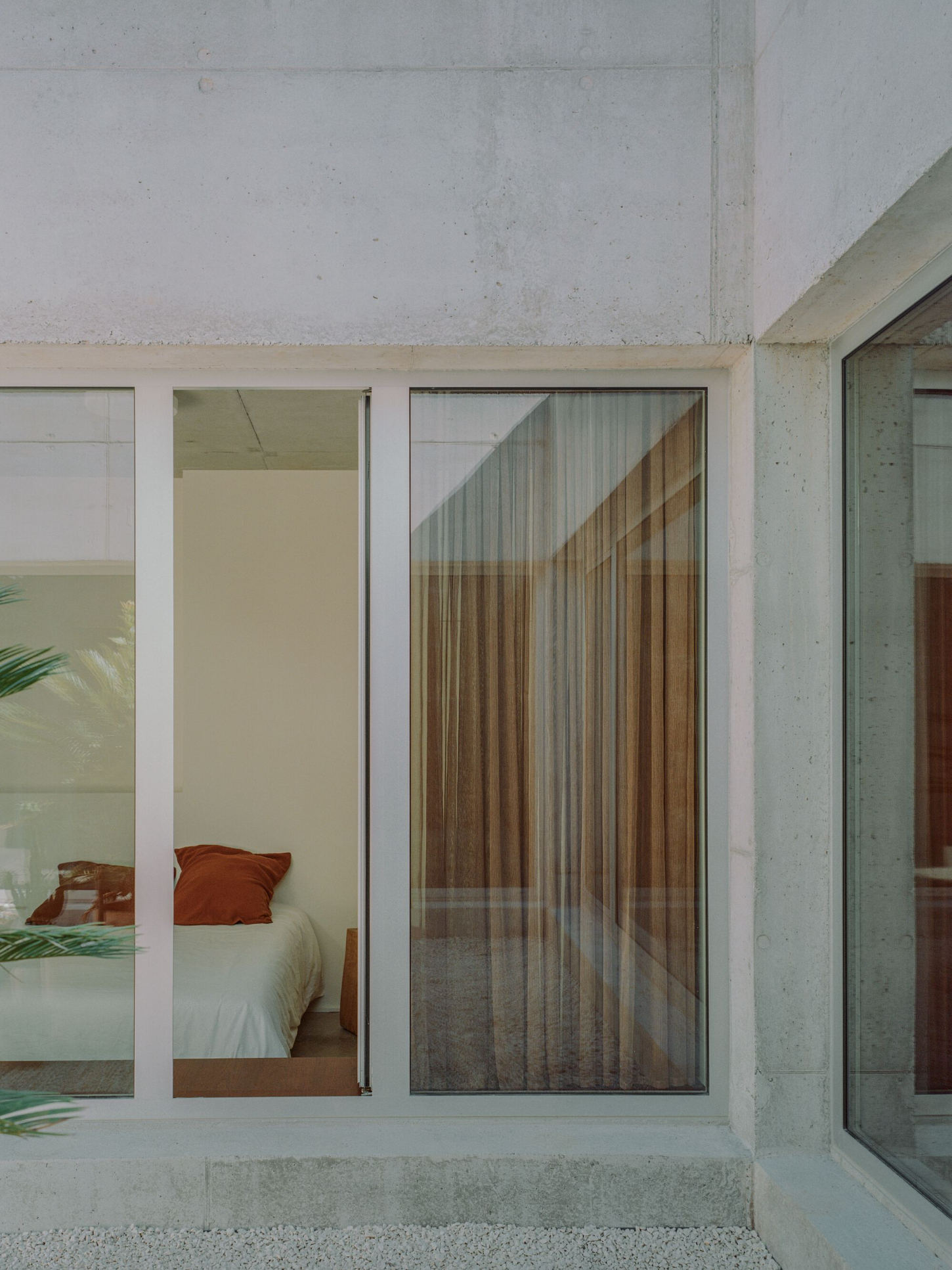 PAYZ House by Alors Studio — A threshold view of a minimally appointed bedroom, framed by an oversized white-bordered glass system that transforms the interior into a contained display.