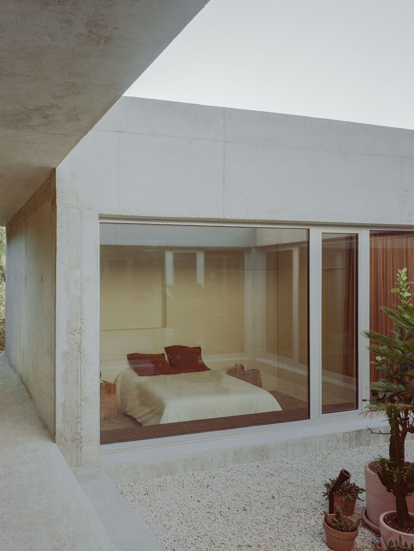 PAYZ House by Alors Studio — A monolithic concrete structure frames an interior bedroom as a framed vignette through oversized glazing.
