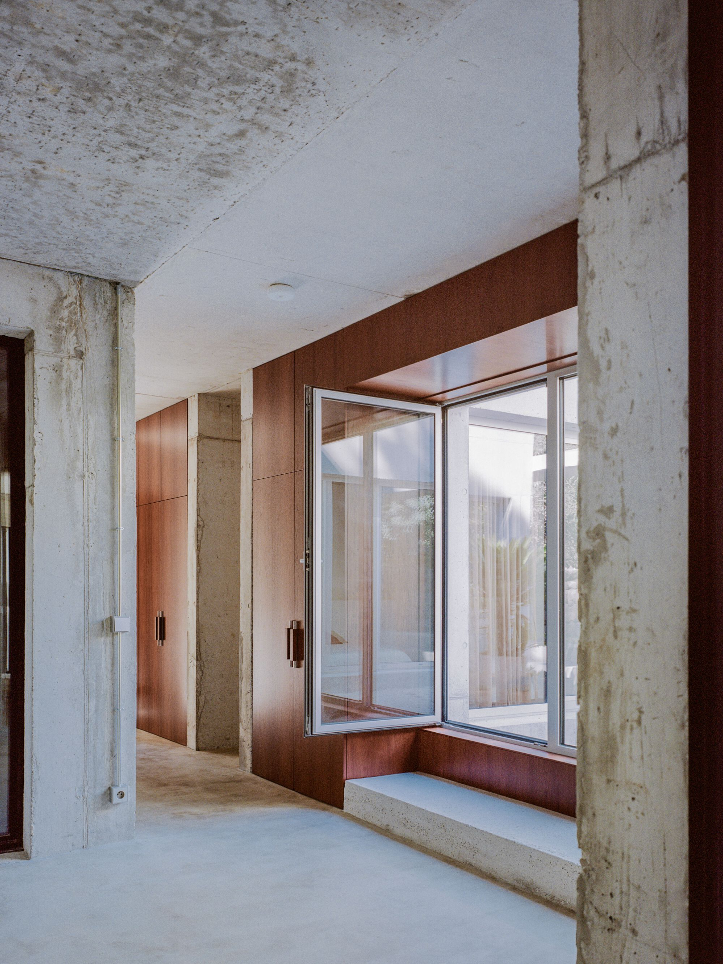 PAYZ House by Alors Studio — A corridor interior frames a bedroom threshold defined by oversized glazed doors and windows with white aluminum frames.