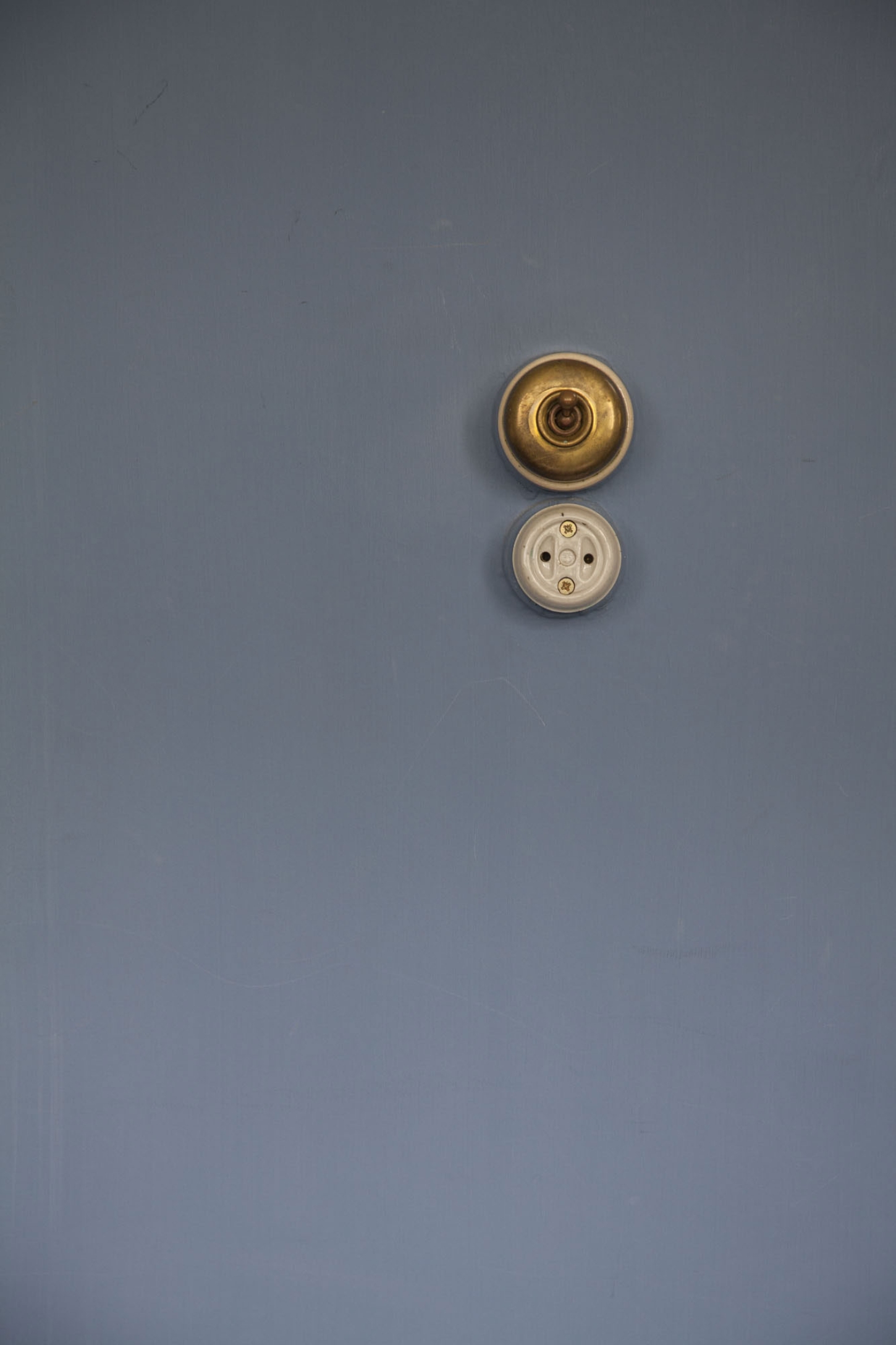 Maison La Roche-Jeanneret by Le Corbusier by Le Corbusier and Pierre Jeanneret — A paired study of brass and cream-colored circular electrical fixtures mounted vertically on a slate-blue wall.