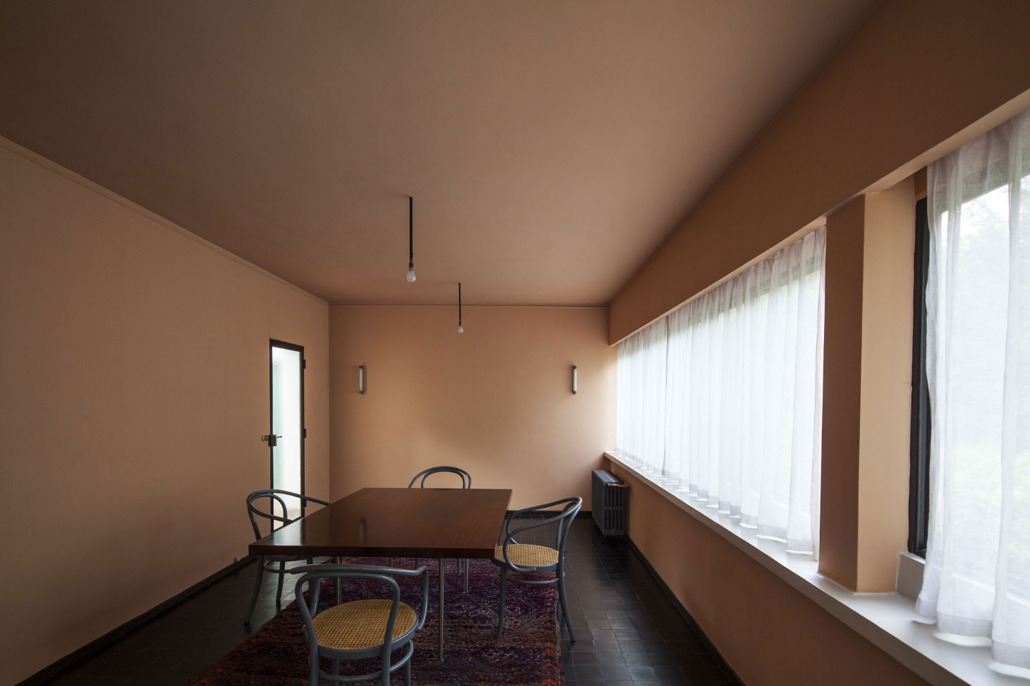 Maison La Roche-Jeanneret by Le Corbusier by Le Corbusier and Pierre Jeanneret — A rectangular dining room with terracotta render walls and matching ceiling, flooded with diffuse light from continuous clerestory windows along the right...