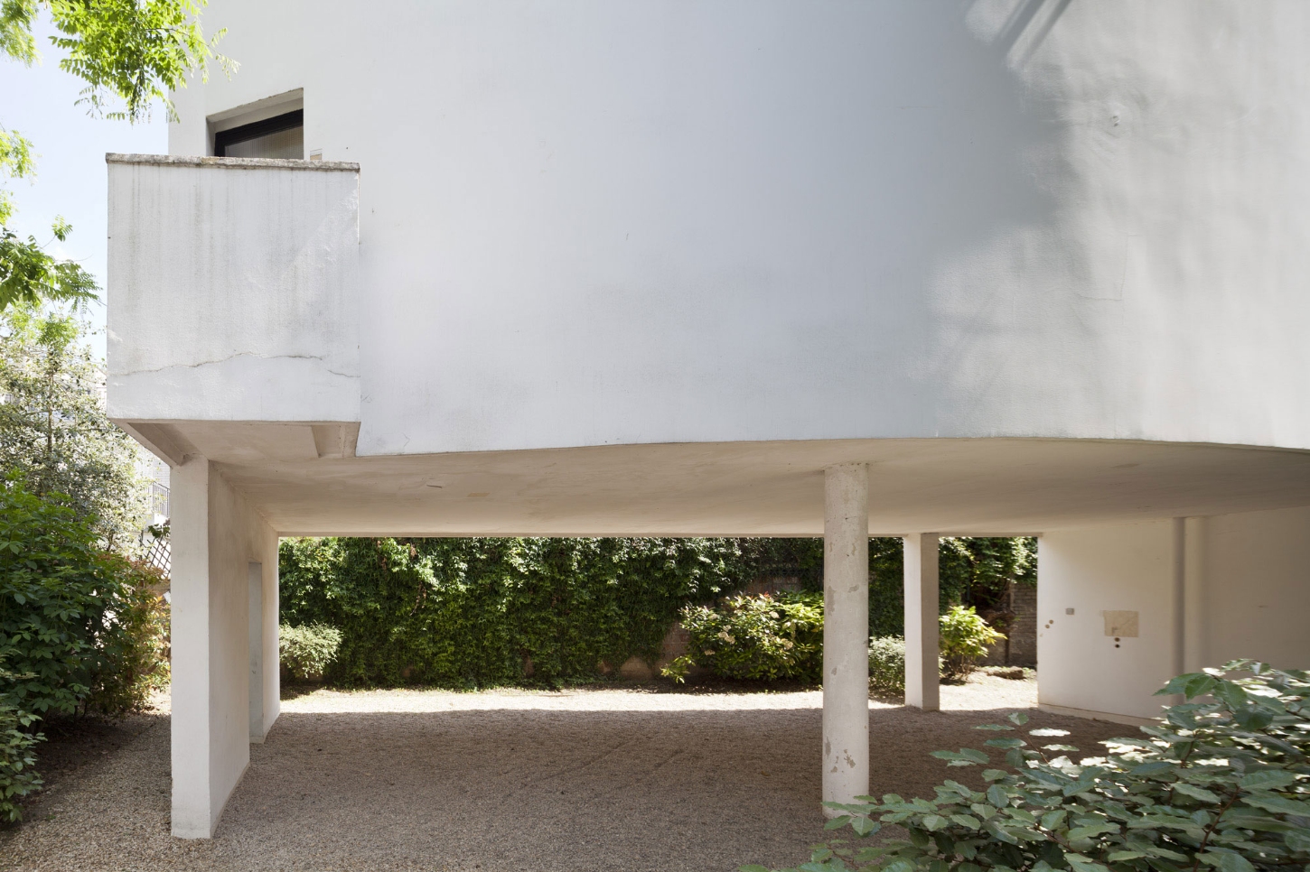 Maison La Roche-Jeanneret by Le Corbusier by Le Corbusier and Pierre Jeanneret — A cantilevered concrete structure extends across a gravel courtyard, its horizontal datum emphasized by white render and supporting cylindrical columns.