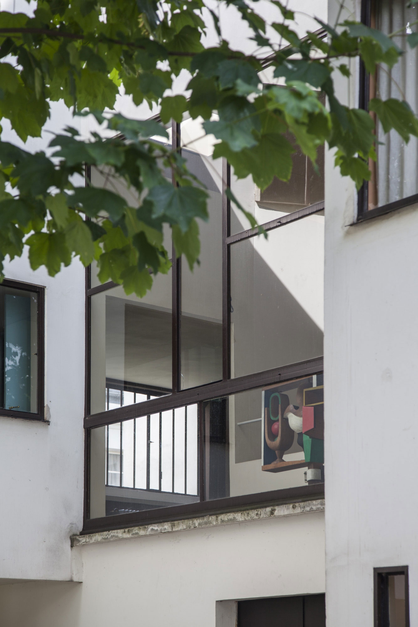 Maison La Roche-Jeanneret by Le Corbusier by Le Corbusier and Pierre Jeanneret — A view into the upper-floor loggia of Maison La Roche, framed by overhanging grapevine foliage.
