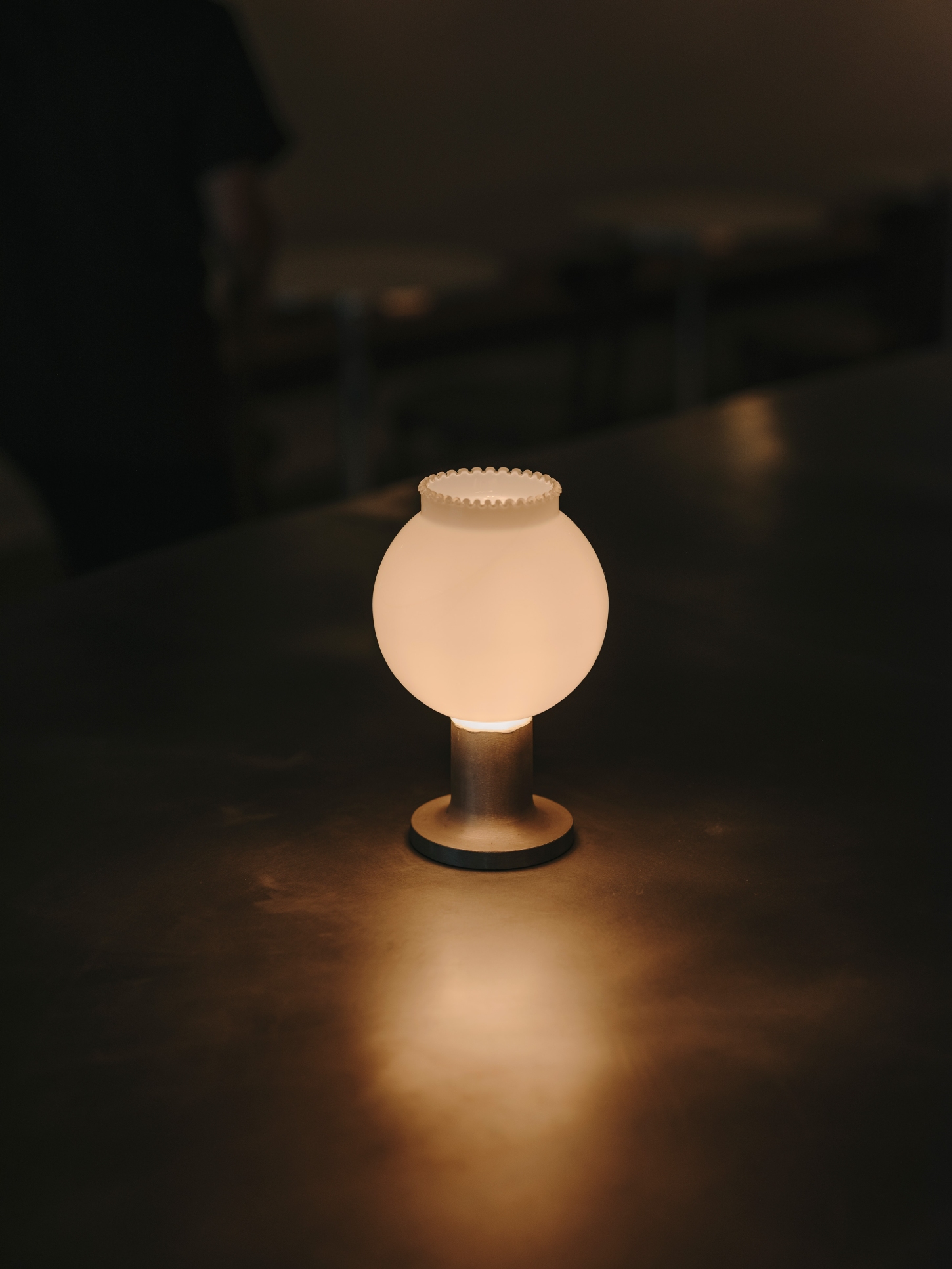 Nomad Coffee Frutas Selectas by Skye Maunsell and Jordi Veciana — A globe pendant light suspends above the curved zinc counter, its frosted glass sphere emitting warm light against the dark interior.