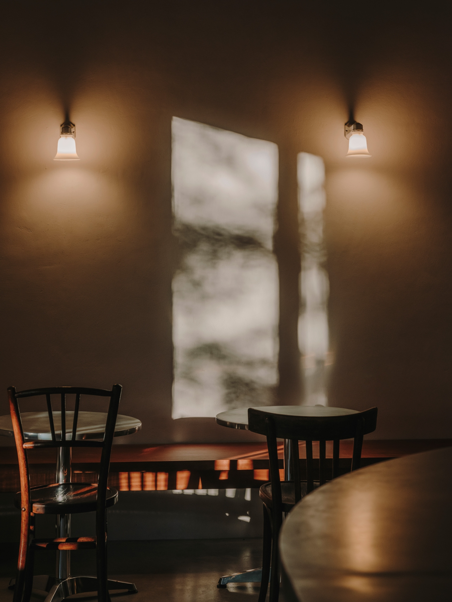 Nomad Coffee Frutas Selectas by Skye Maunsell and Jordi Veciana — A dining zone bathed in warm pendant light from two brass-mounted fixtures with milk-glass shades.