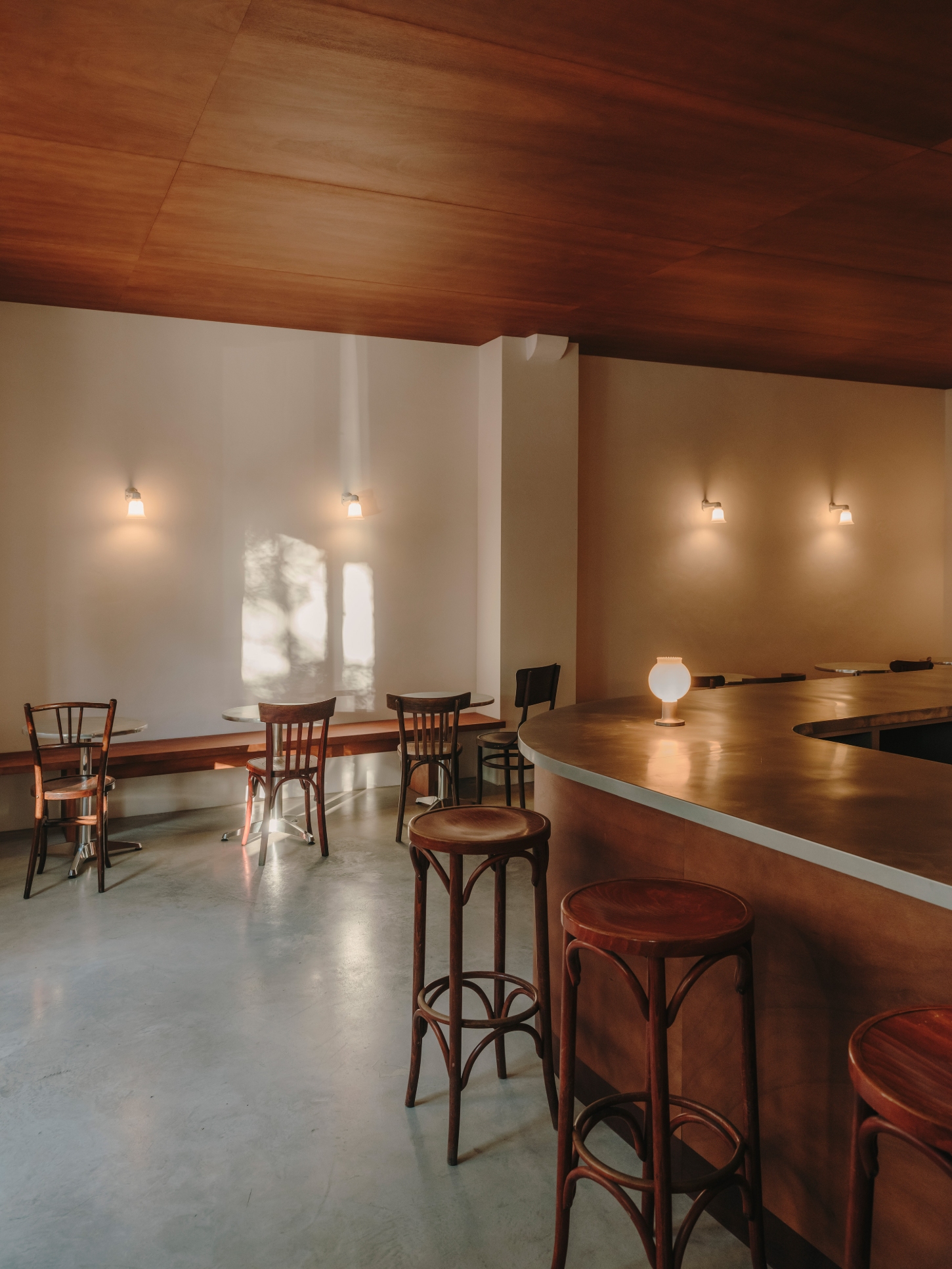 Nomad Coffee Frutas Selectas by Skye Maunsell and Jordi Veciana — The dining zone anchors the space with bentwood café chairs positioned at small round tables across a polished concrete floor.