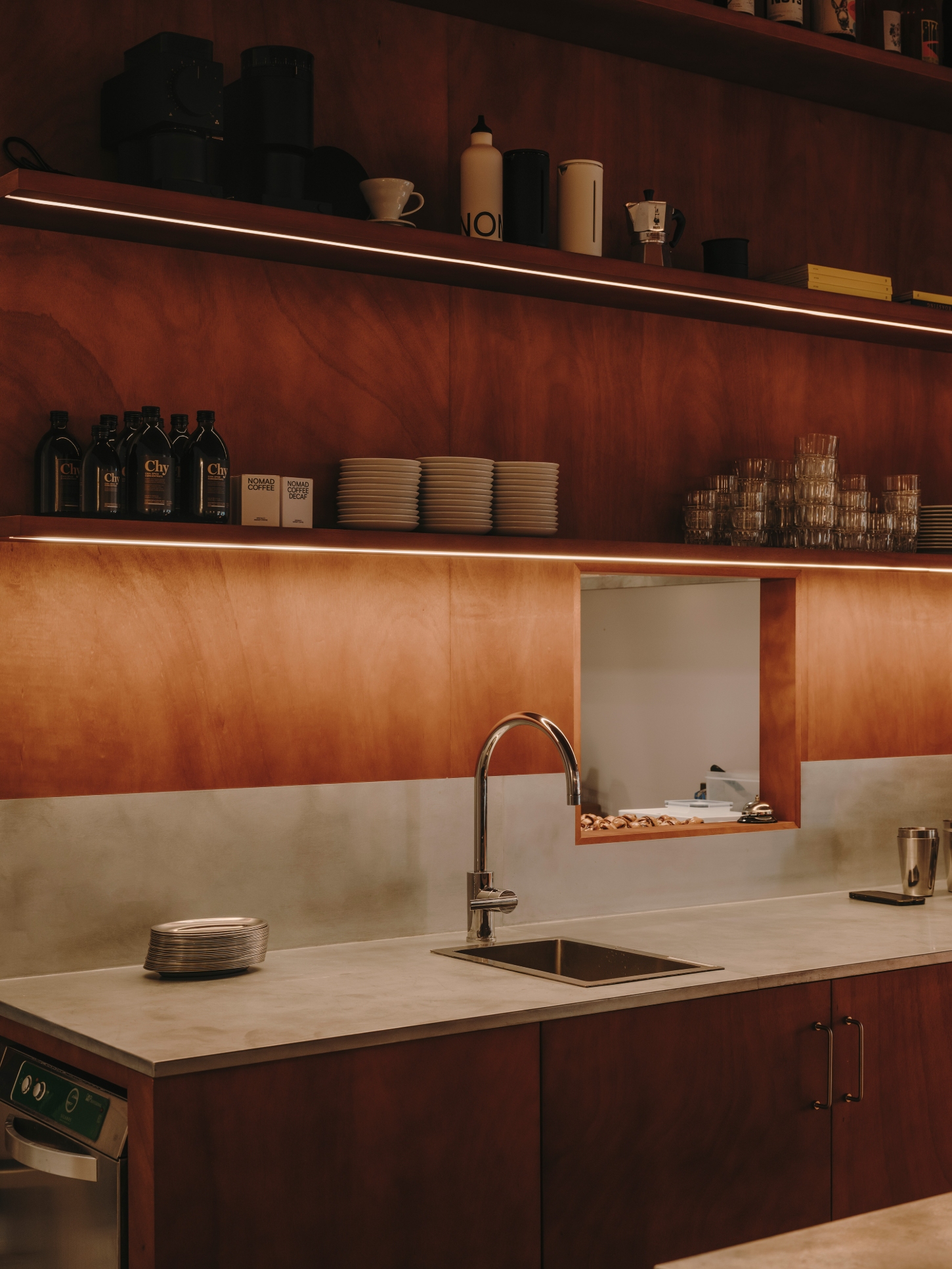 Nomad Coffee Frutas Selectas by Skye Maunsell and Jordi Veciana — A service counter positioned against a bipartite wall of terracotta render above and cream plaster below, divided by a horizontal steel shelf with...