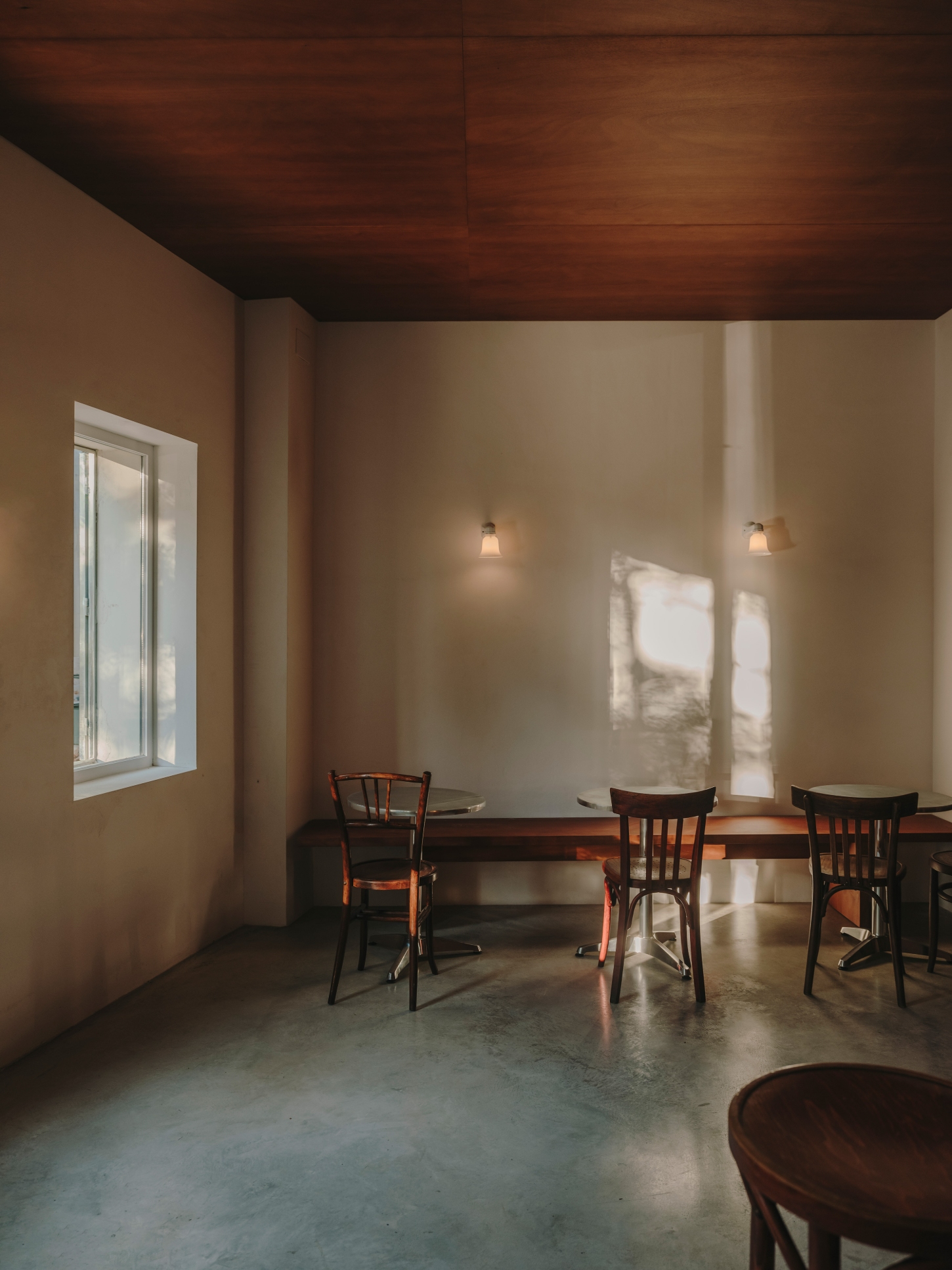 Nomad Coffee Frutas Selectas by Skye Maunsell and Jordi Veciana — A dining zone captured in golden-hour light, where three bentwood café chairs surround a dark timber table positioned beneath two wall-mounted pendant lights.