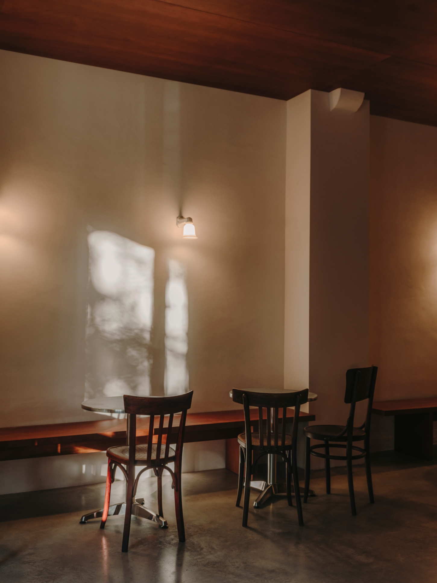 Nomad Coffee Frutas Selectas by Skye Maunsell and Jordi Veciana — Three bentwood café chairs cluster around a small table in the dining zone, their dark-stained frames casting shadows on the polished concrete floor.