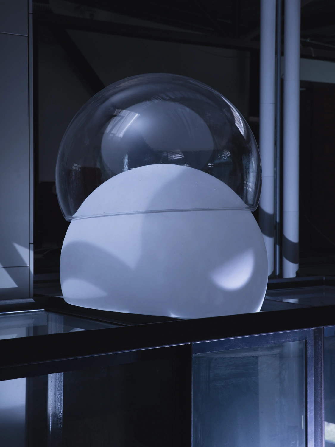 Protege Noctem by Mattia Balsamini & Raffaele Panizza — A sculptural intervention in a gallery or museum setting, featuring a semi-translucent dome of dark-tinted glass positioned over a white, organic form.