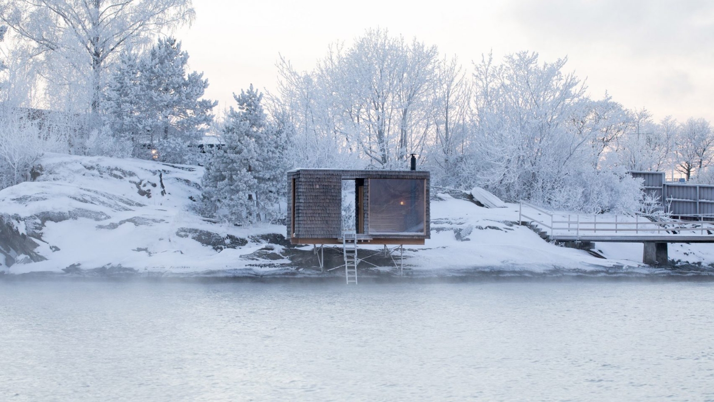 The Hotspot Oslo Works — A compact sauna structure elevated on wooden stilts extends into frozen water on the Nesodden Peninsula.