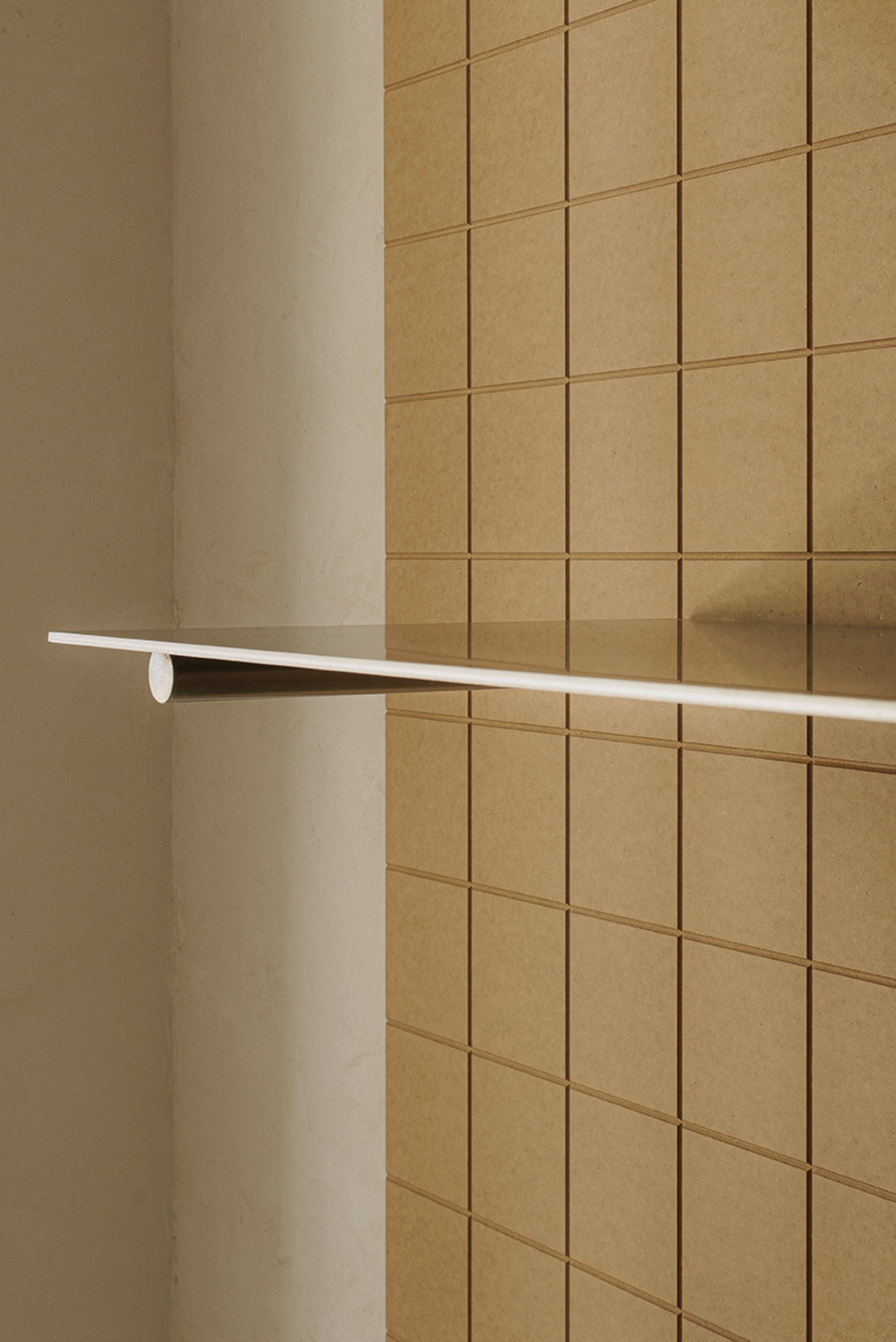 Madreamiga Madrid by estudio DIIR — A detail shot isolates a single horizontal stainless steel shelf mounted against a gridded terracotta tile wall.