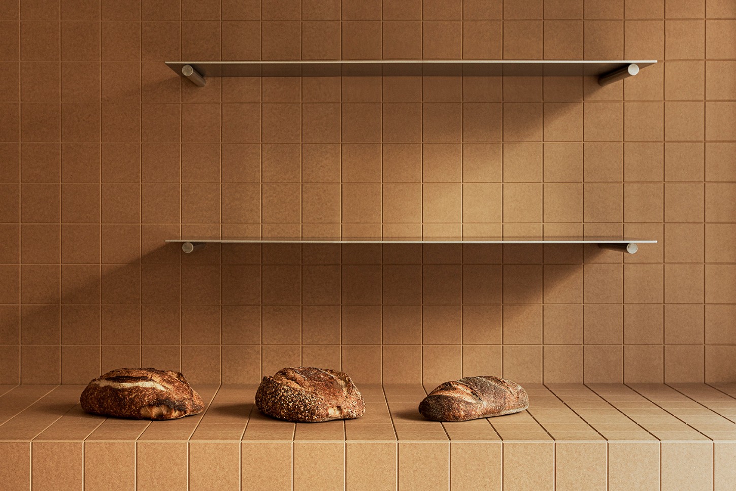 Madreamiga Madrid by estudio DIIR — Three artisan sourdough loaves sit on a tiled floor beneath two cantilevered stainless steel shelves.