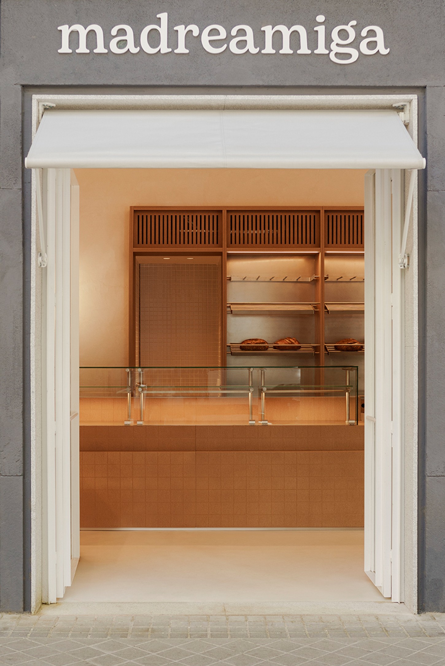 Madreamiga Madrid by estudio DIIR — Madreamiga's display counter features a gridded terracotta tile wall in uniform small squares, creating a textured backdrop for the merchandising zone.