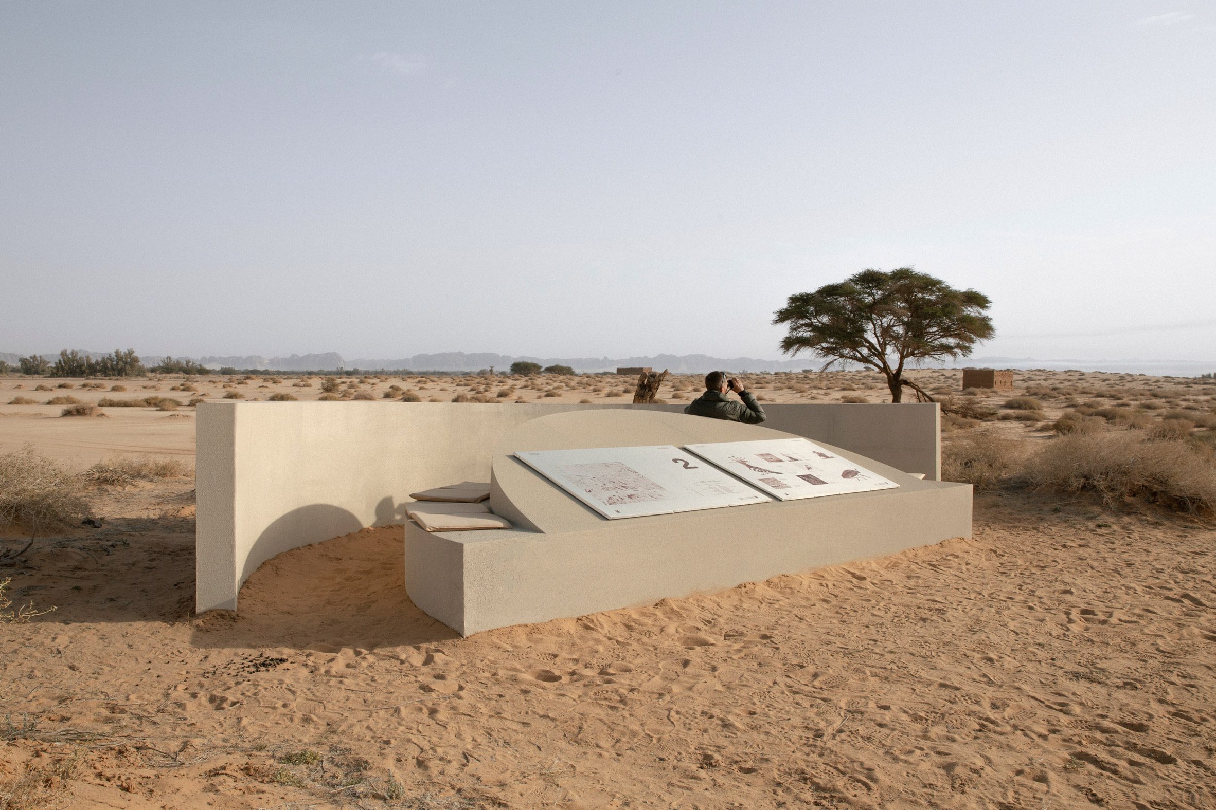 Hegra Viewpoints AlUla desert by Clover Studio — A cream-rendered concrete structure with curved walls anchors the desert landscape, its billowing white fabric canopy tensioned overhead.