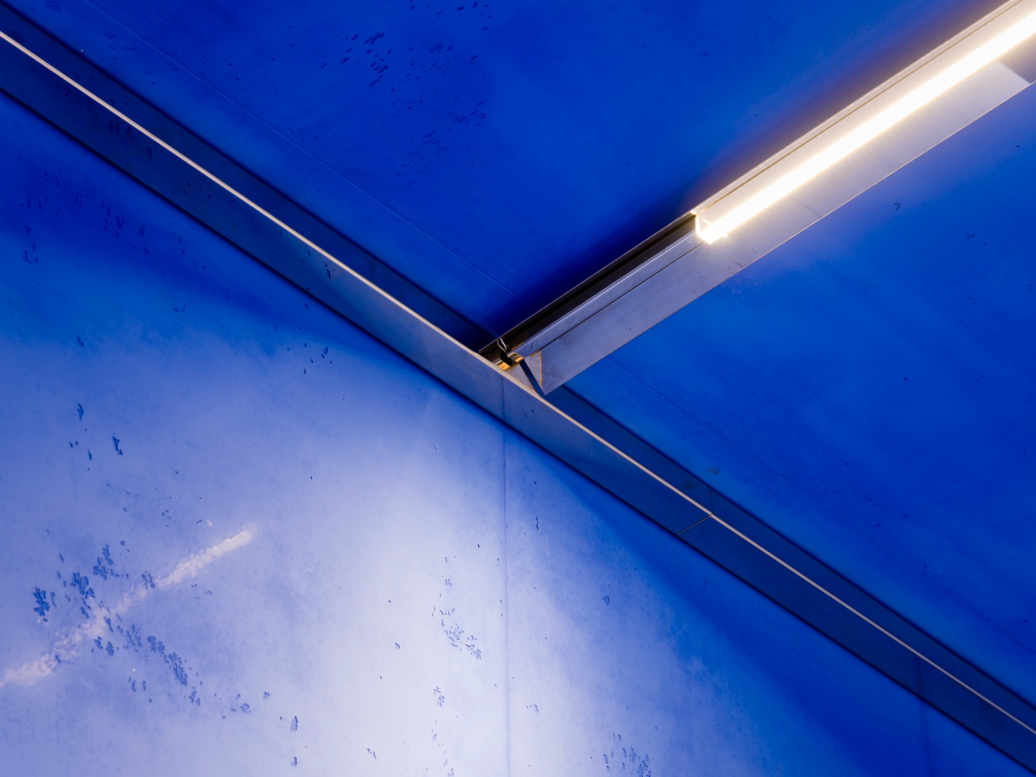 Aera Bakery by Gonzalez Haase AAS — A linear LED strip fixture runs horizontally along the ceiling edge, its white fluorescent glow contrasting sharply against the monochromatic lapis lazuli...