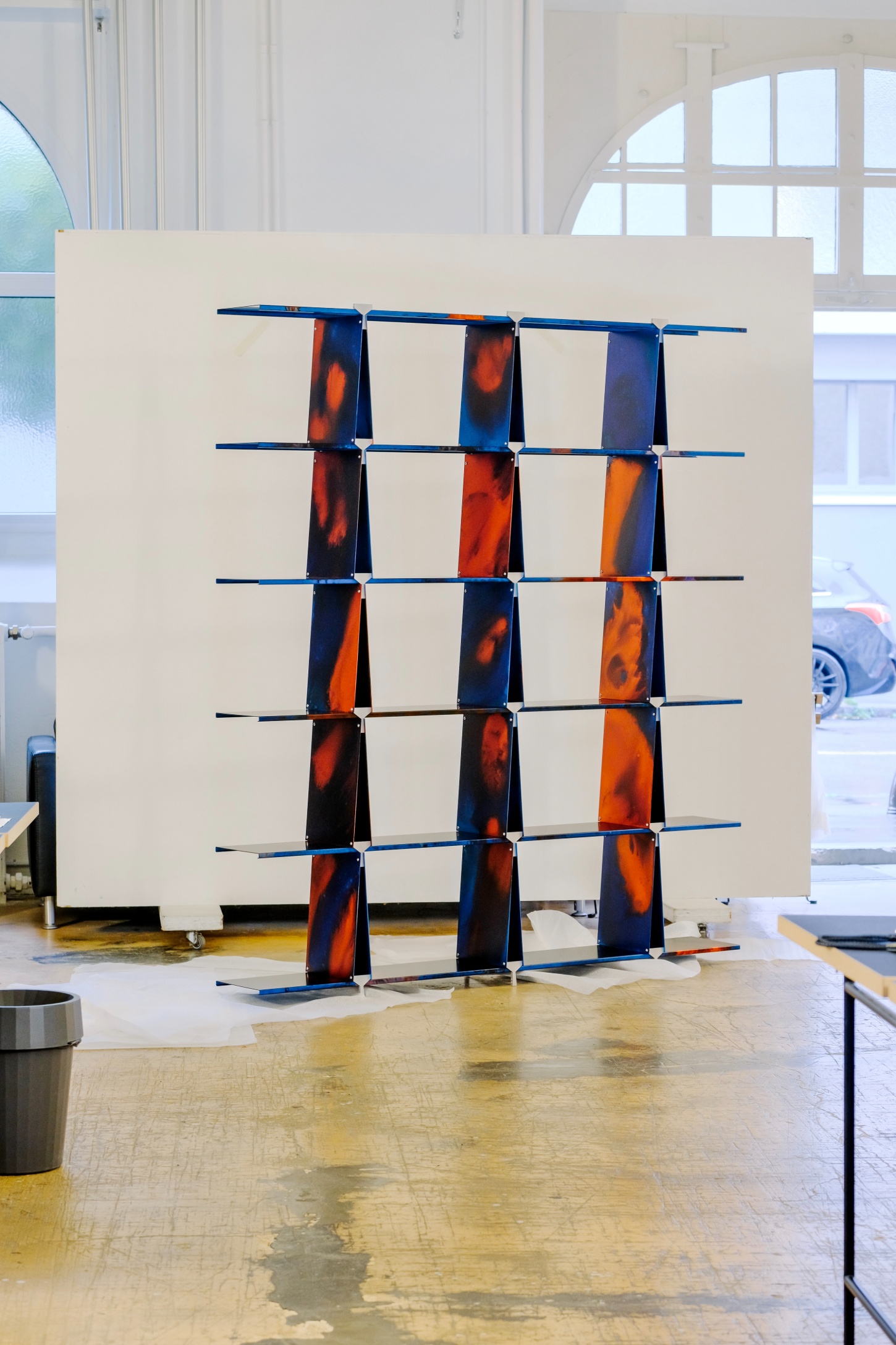 ‘Philae’ by Raphael Kadid — Philae presents a 3×3 grid of hand-anodized aluminum panels suspended between horizontal blue metal rods in a bright gallery setting.