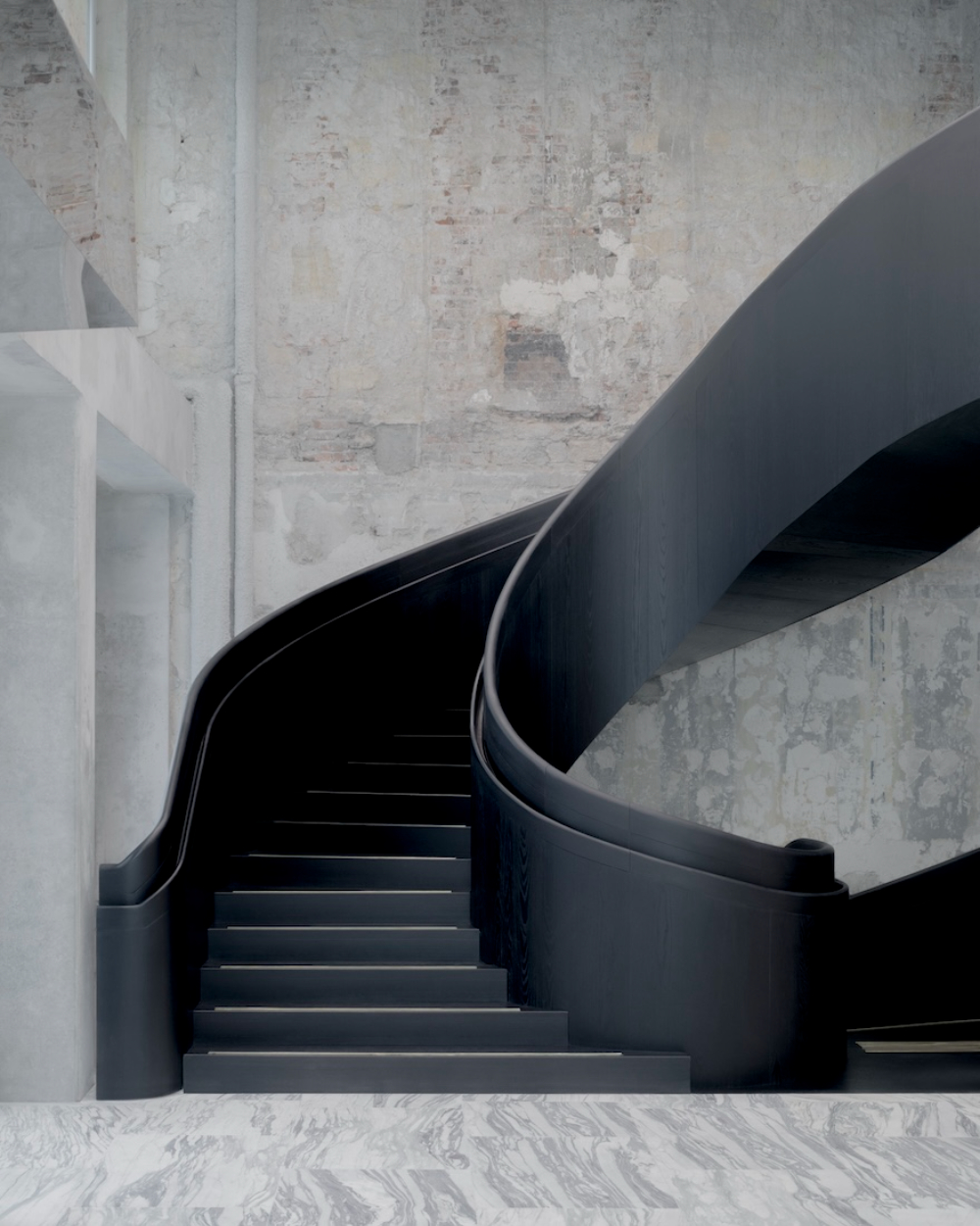 Saint Laurent Flagship in Paris by Sain Laurent — A black-lacquered steel staircase descends into the flagship's lower level, its continuous curved handrail sweeping in sculptural counterpoint to the...