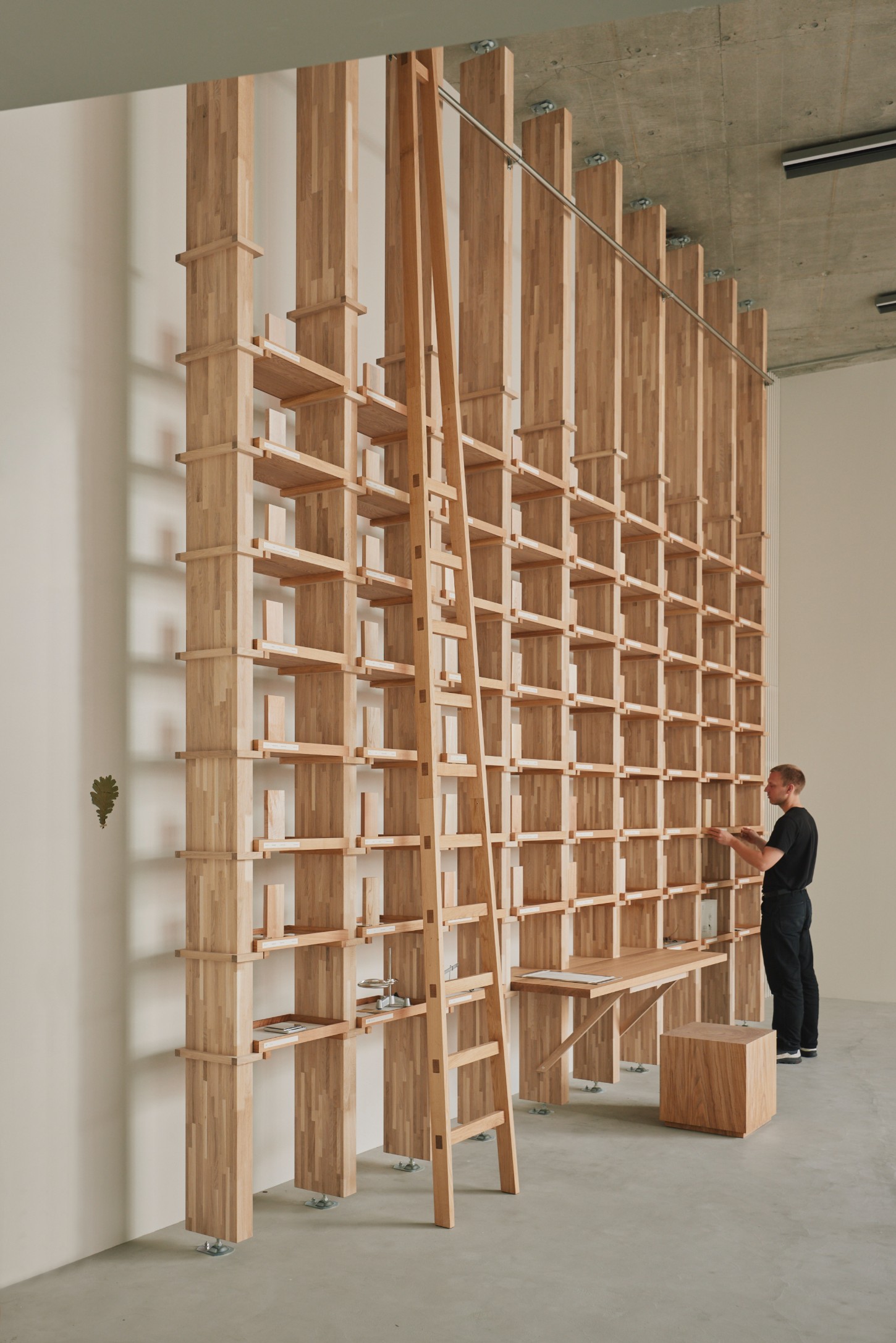 'The Age of Wood' by CHRISTIAN + JADE in Karimoku Research — A monumental timber grid-wall installation dominates the gallery space, constructed from vertical timber posts with horizontal shelving elements creating...