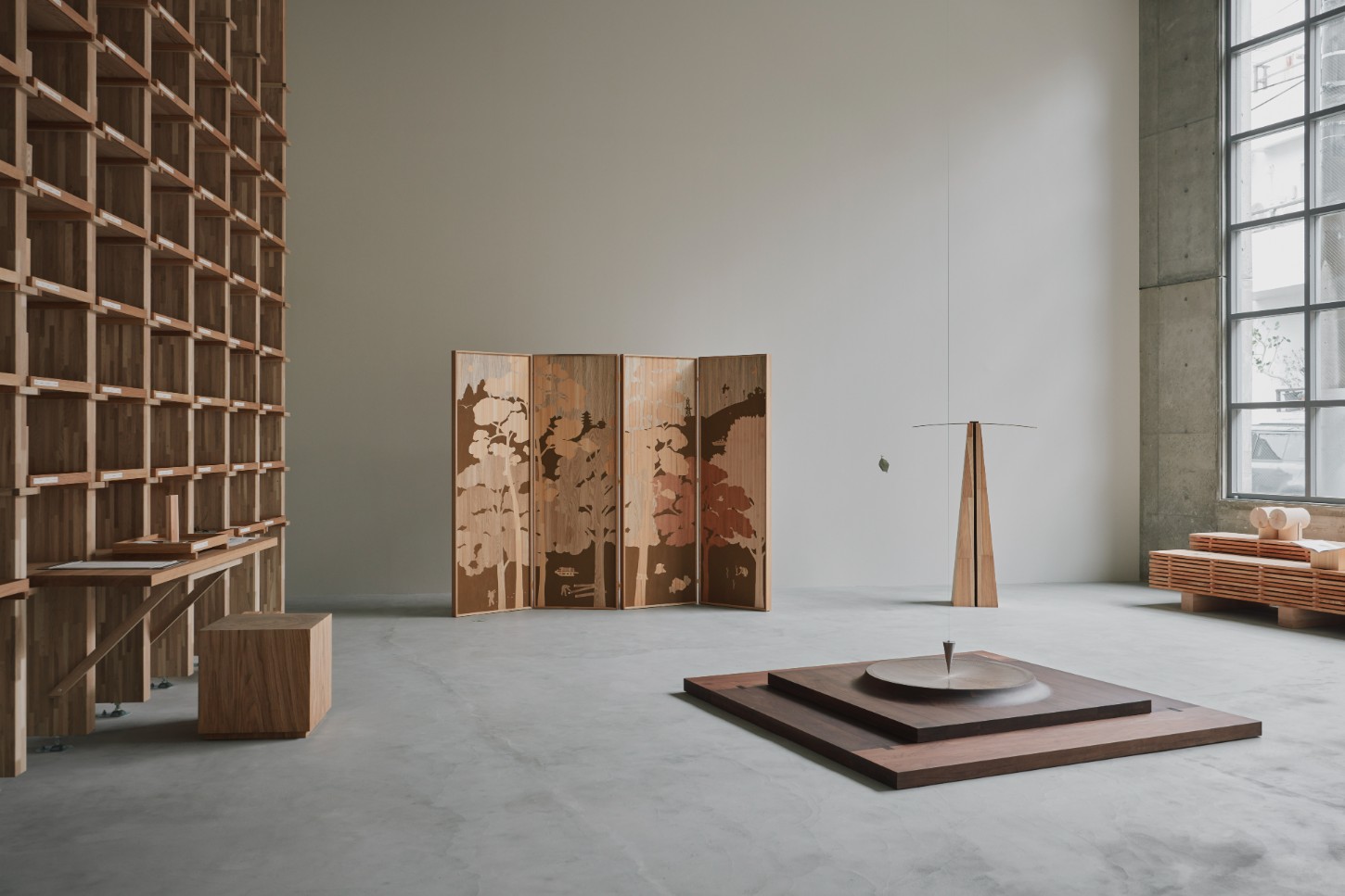 'The Age of Wood' by CHRISTIAN + JADE in Karimoku Research — The exhibition space features a four-panel folding screen as the primary focal point, its timber panels inlaid with botanical silhouettes in contrasting...