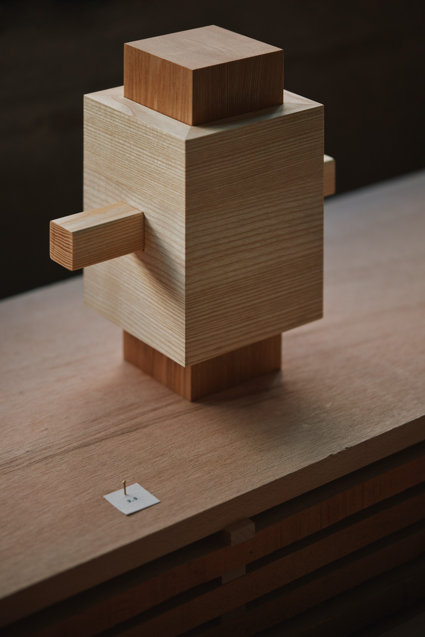 'The Age of Wood' by CHRISTIAN + JADE in Karimoku Research — A sculptural timber assembly occupies the center of a wooden platform, composed of stacked geometric blocks in contrasting wood tones.