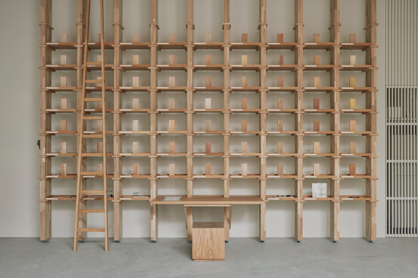 'The Age of Wood' by CHRISTIAN + JADE in Karimoku Research — A monumental timber grid-wall occupies the gallery expanse, its repetitive square compartments creating a rhythmic void pattern across the full height of...