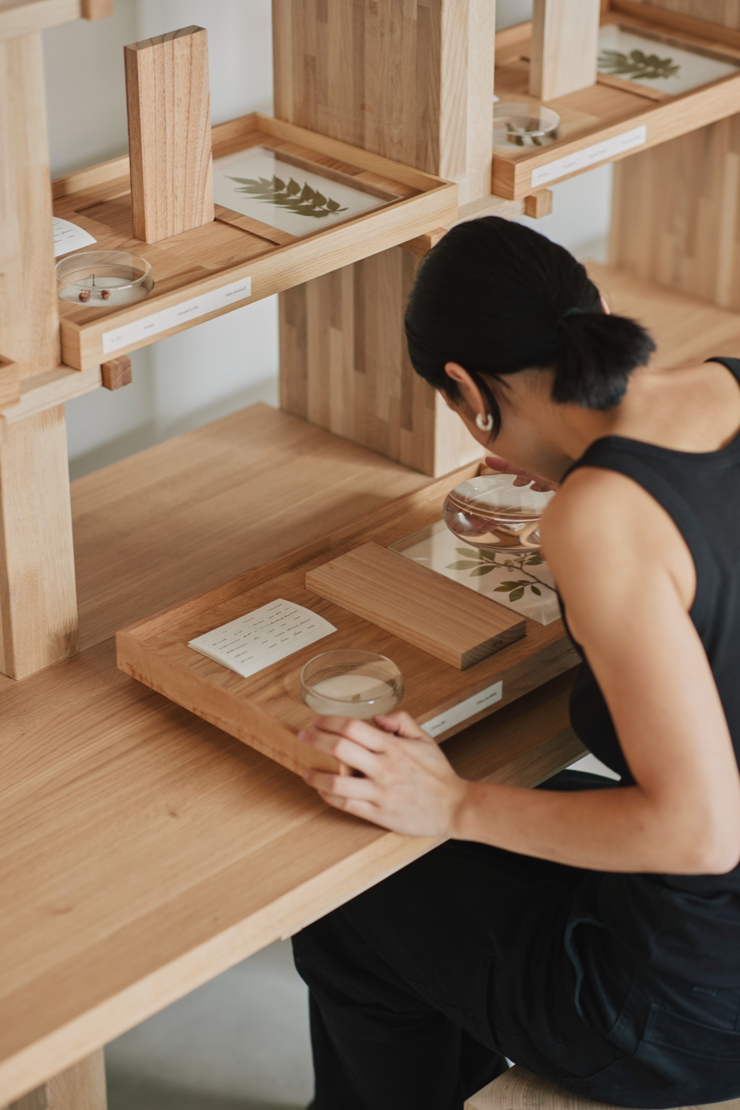 'The Age of Wood' by CHRISTIAN + JADE in Karimoku Research — A person examines a timber shelving system designed with open square compartments creating a rhythmic void pattern.