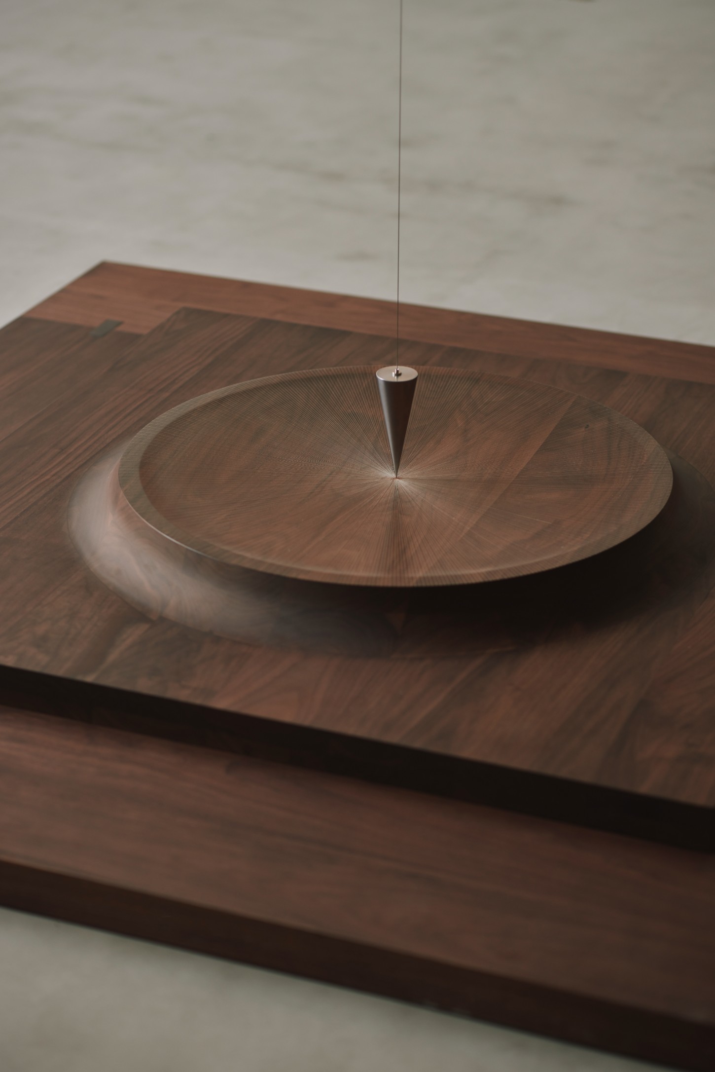 'The Age of Wood' by CHRISTIAN + JADE in Karimoku Research — A wooden vessel sits centered on a walnut-stained timber platform, its concentric circular grain pattern emphasizing radial geometry.