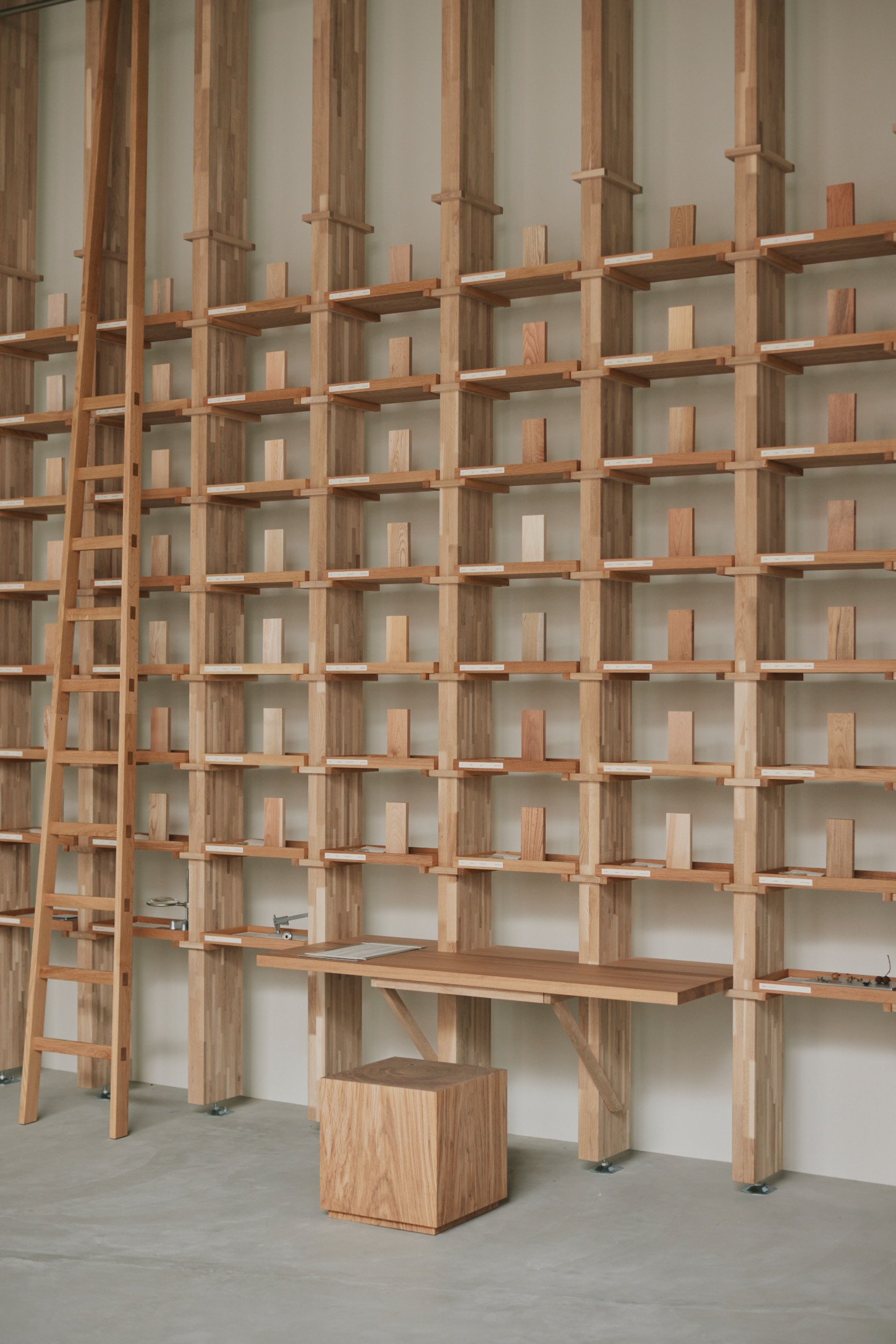 'The Age of Wood' by CHRISTIAN + JADE in Karimoku Research — A timber grid-wall system dominates the exhibition space, composed of vertical posts and horizontal shelving elements organized into a modular matrix of...