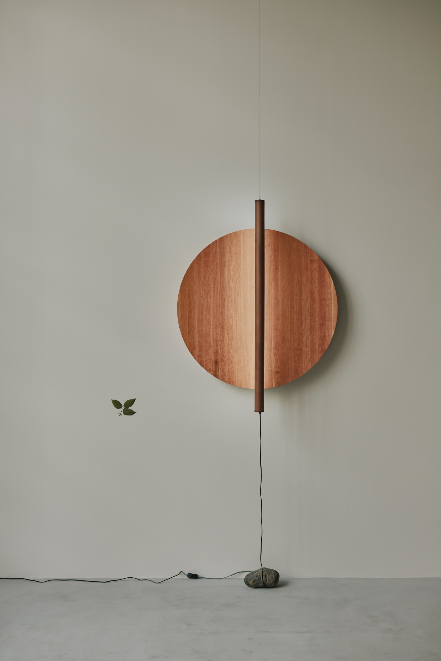 'The Age of Wood' by CHRISTIAN + JADE in Karimoku Research — A sculptural timber installation suspended against a neutral wall features a circular wooden disc in warm honey tones, bisected by a dark cylindrical wooden...