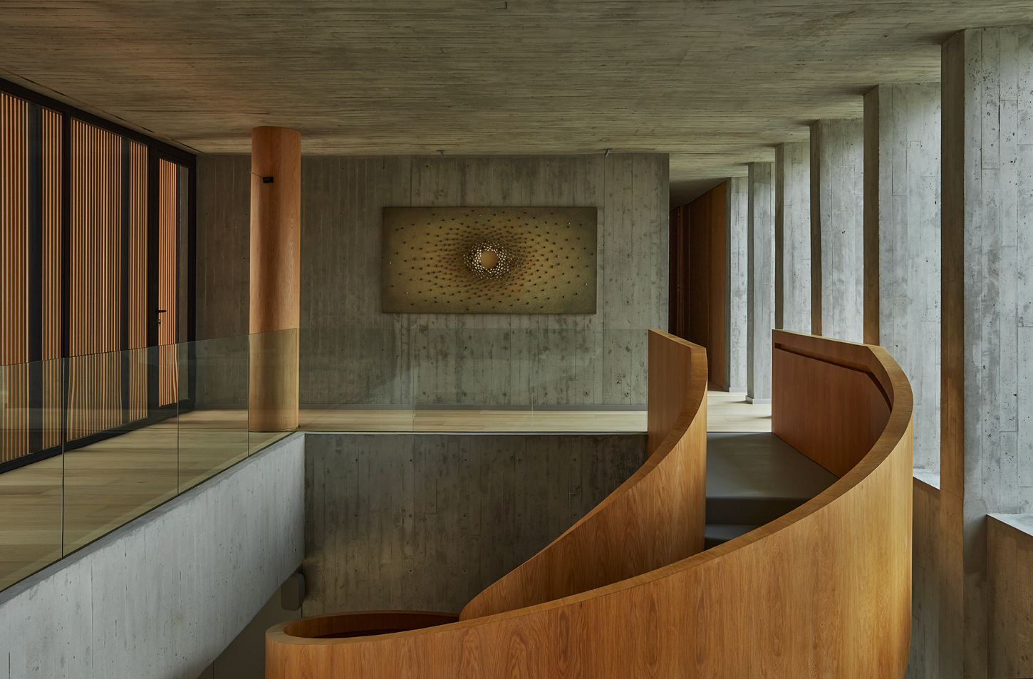 Casa Haras by 5Solidos — A double-height interior volume showcases a sculptural helical timber staircase in warm oak, its continuous curved form dominating the composition.