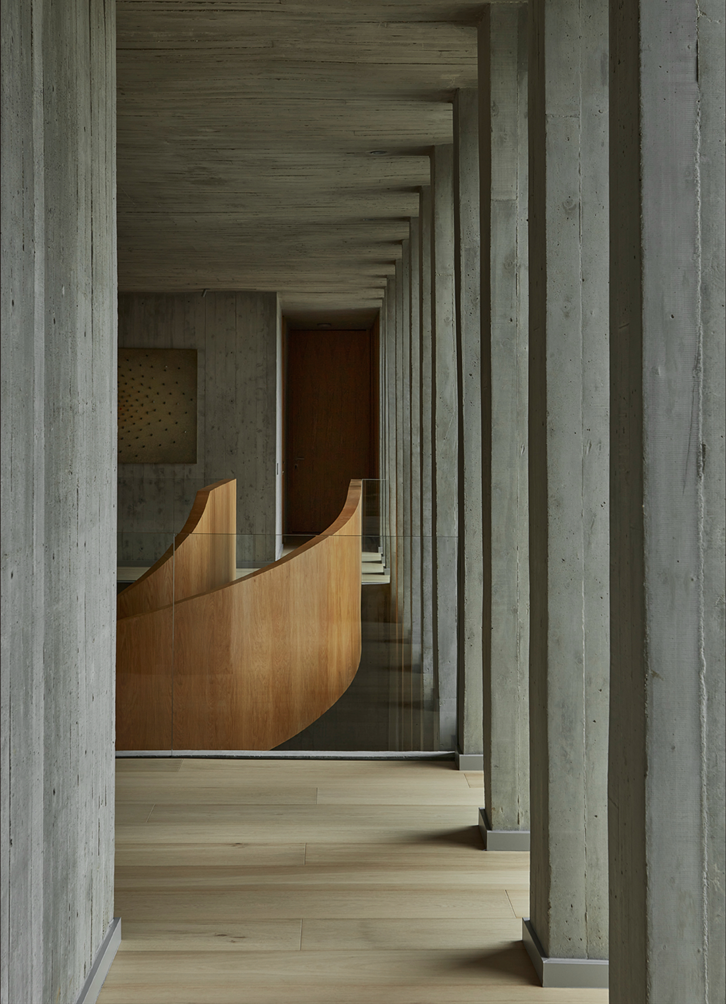 Casa Haras by 5Solidos — A receding corridor framed by board-formed concrete columns creates linear perspective toward a timber reception desk.