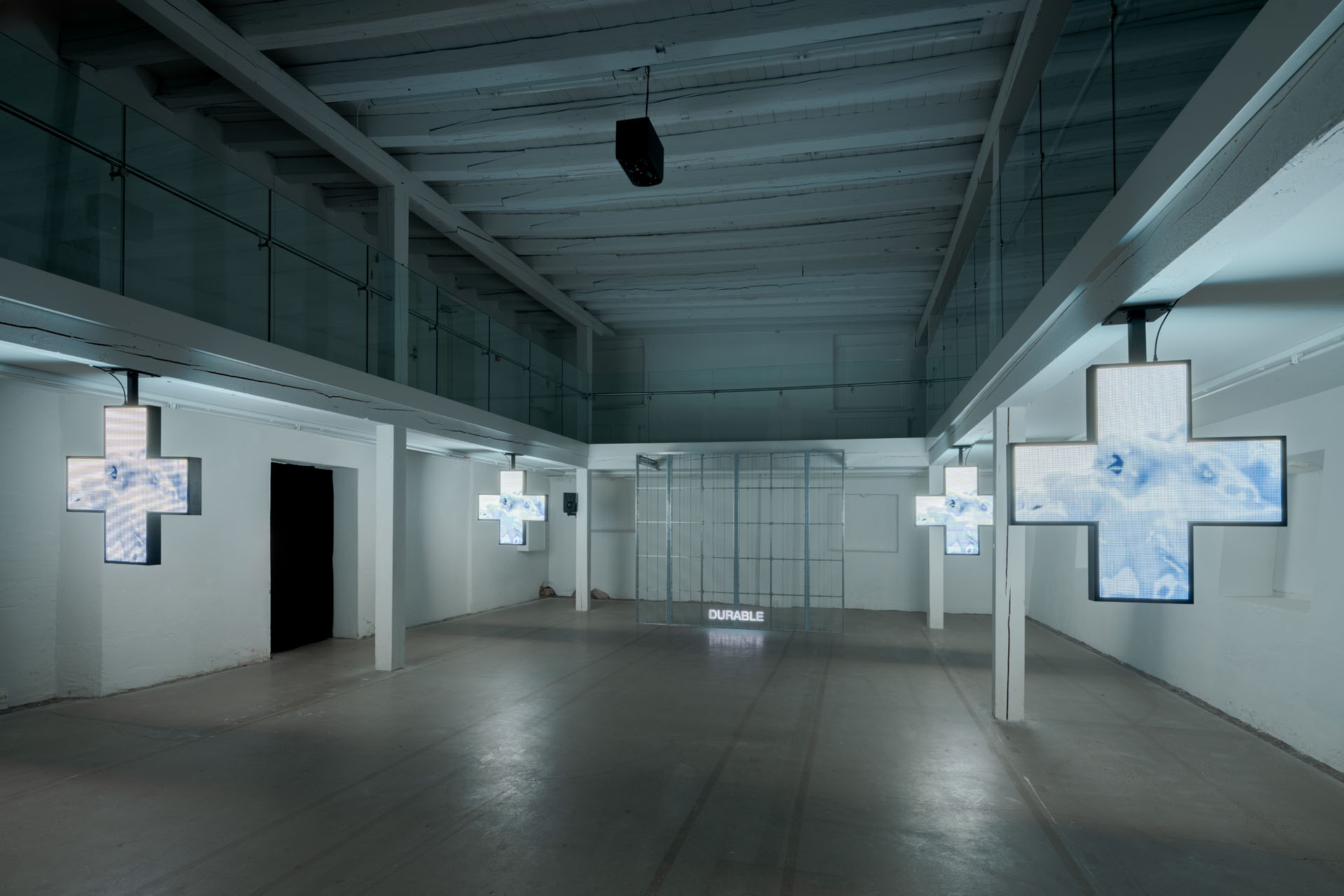 Milk Plus by Jens Settergren Viborg Kunsthal — A multiplex video installation spans the industrial gallery floor, with cross-shaped LED screens suspended from the concrete ceiling displaying...