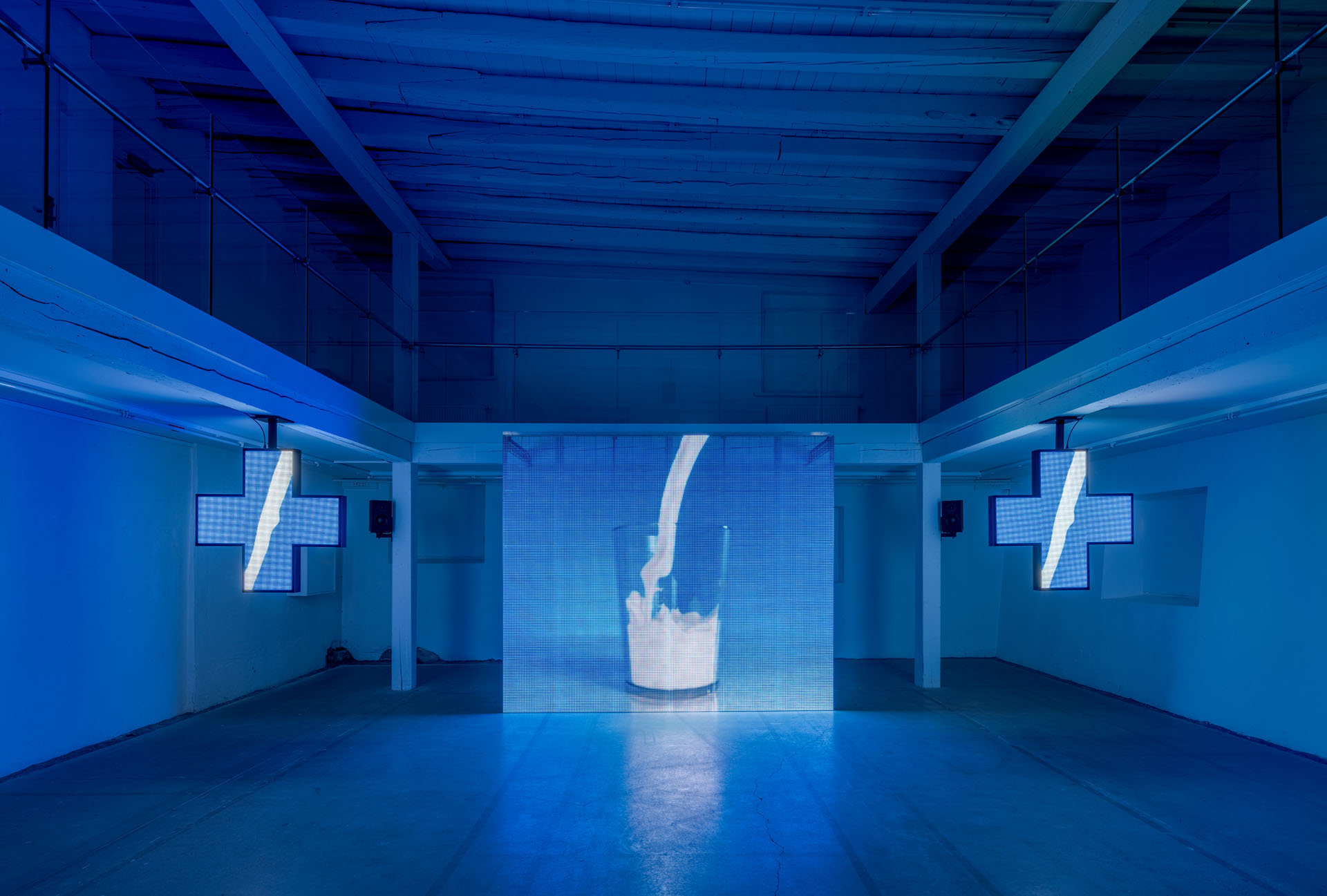 Milk Plus by Jens Settergren Viborg Kunsthal — A video installation occupies the center of a monolithic blue gallery space, its LED pixel grid displaying a low-resolution image of milk being poured into...