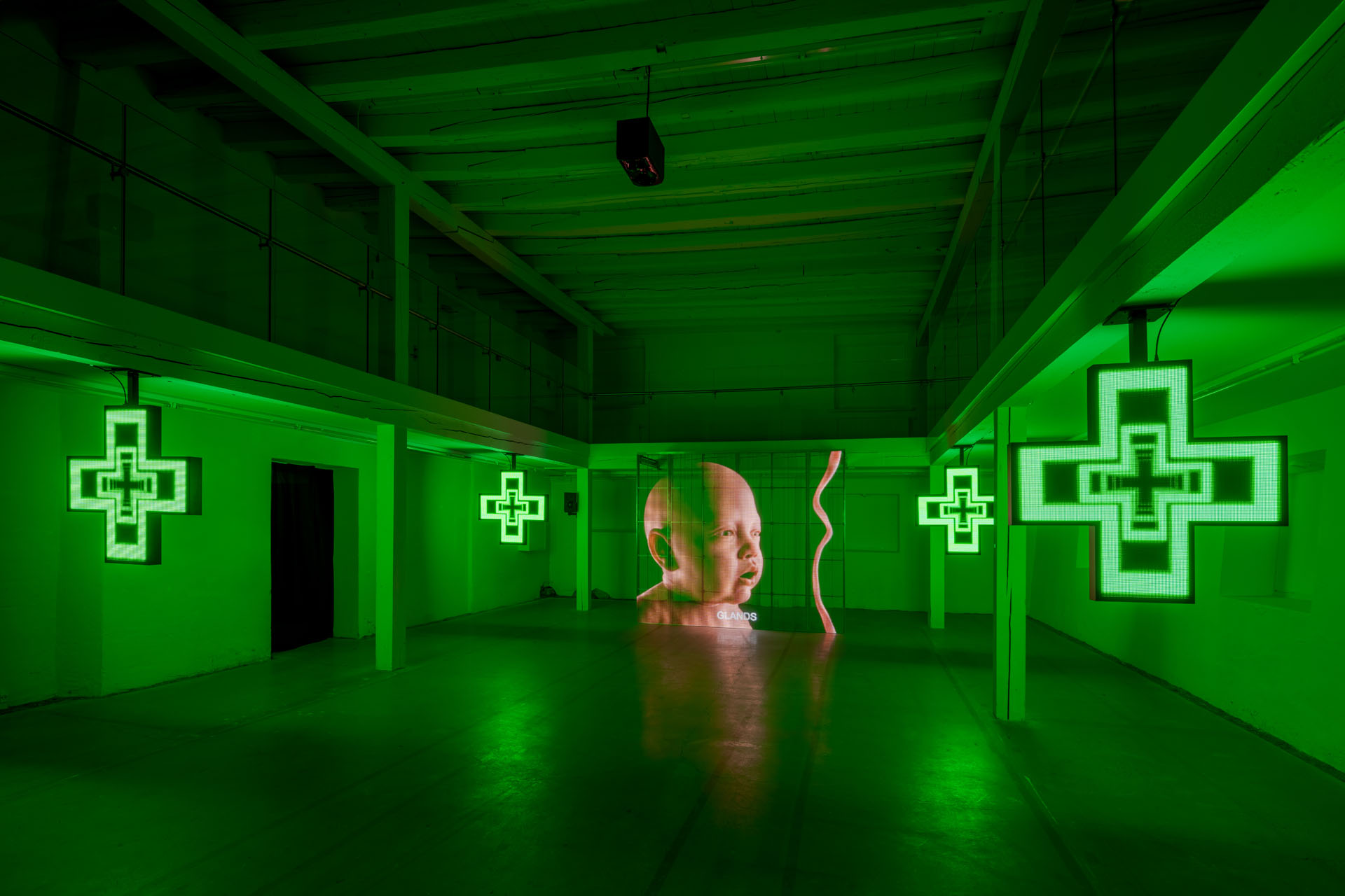 Milk Plus by Jens Settergren Viborg Kunsthal — A monolithic LED screen dominates the industrial gallery space, displaying a low-resolution pixelated portrait of a bald infant's head in warm peachy tones...