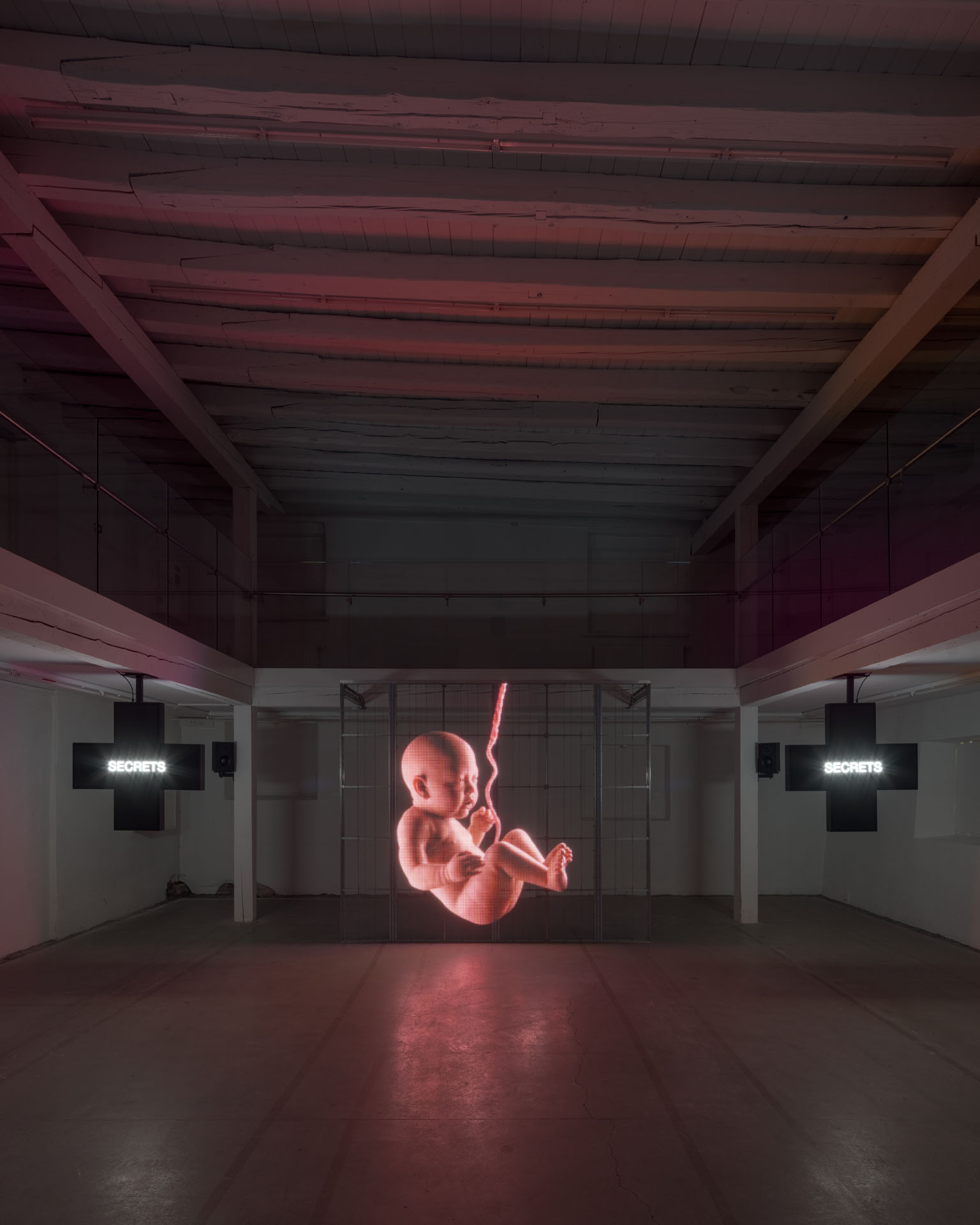 Milk Plus by Jens Settergren Viborg Kunsthal — A large-scale LED pixel grid display dominates the industrial gallery space, emitting a monochromatic red light that renders a low-resolution fetal form in...