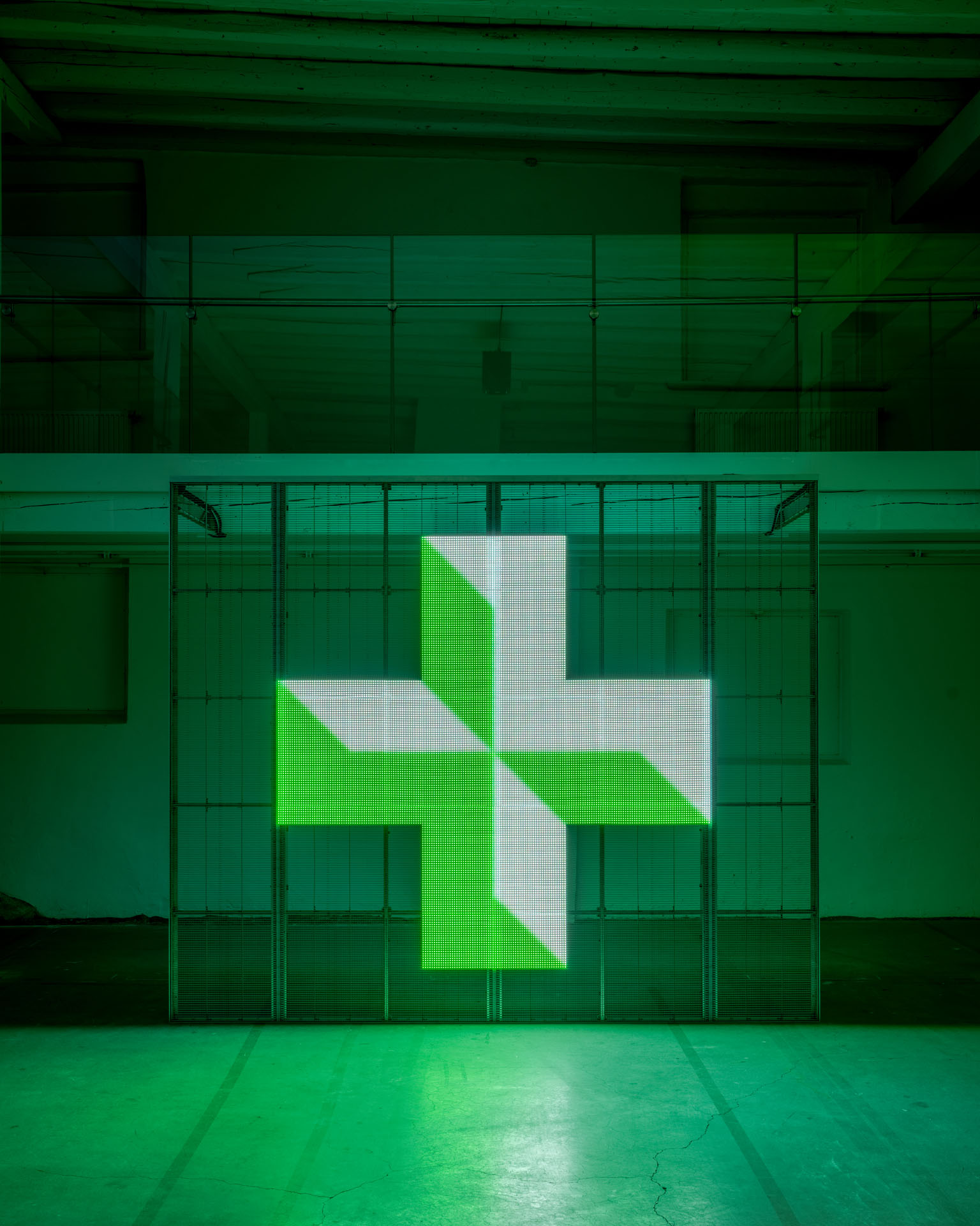 Milk Plus by Jens Settergren Viborg Kunsthal — A freestanding LED pixel display dominates the industrial gallery interior, presenting a geometric cross motif in bright lime-green and white pixels against...