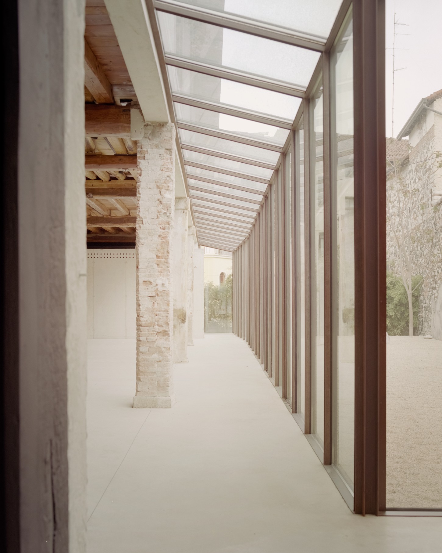 Atipografia Threshold and Treasure Gallery by AMAA — A linear passage framed by floor-to-ceiling glazing on the right, with timber mullions defining a rhythmic grid of transparent panels.