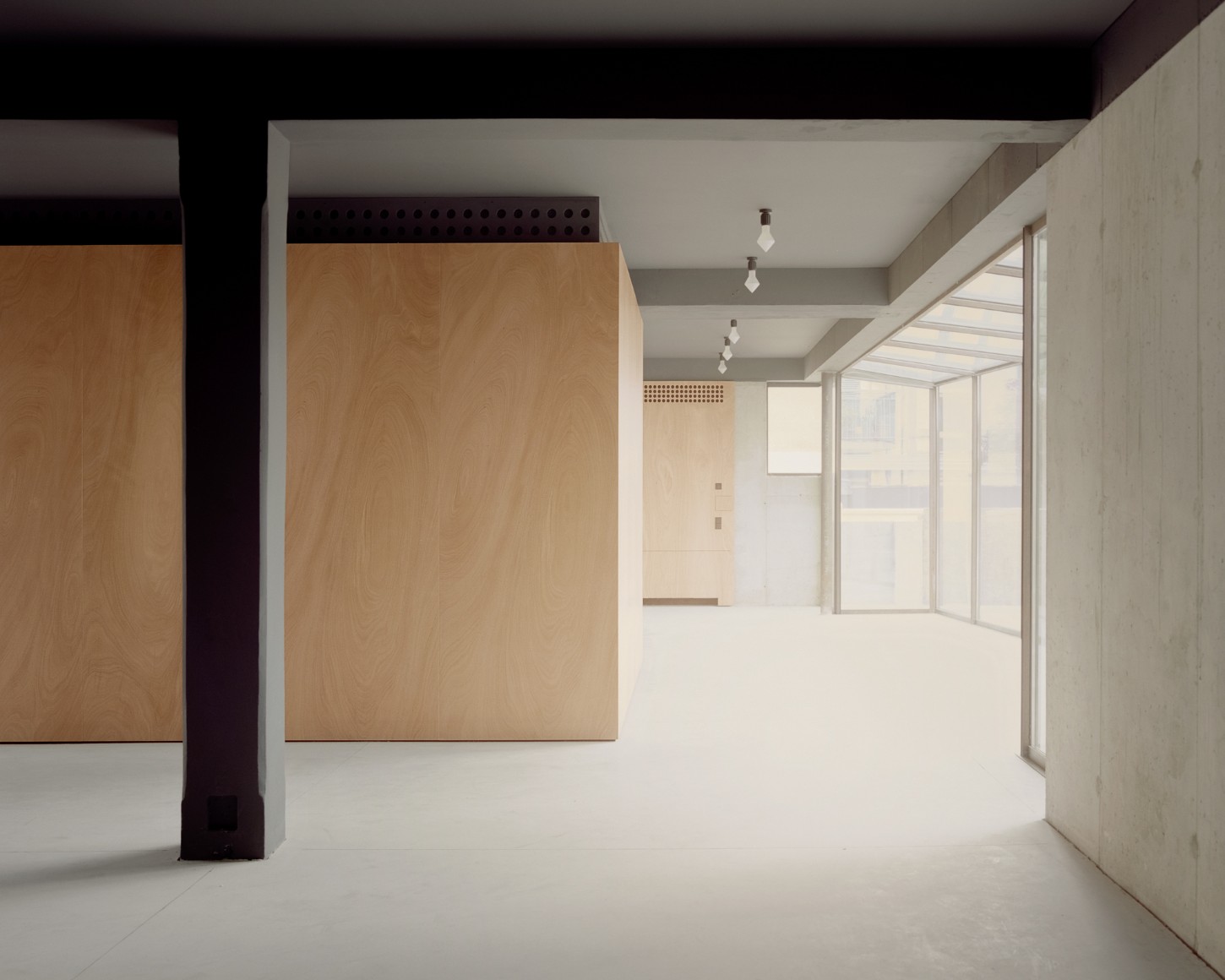 Atipografia Threshold and Treasure Gallery by AMAA — The gallery interior reveals a sequence of thresholds defined by large-scale plywood panels in warm honey tones, positioned asymmetrically within a...