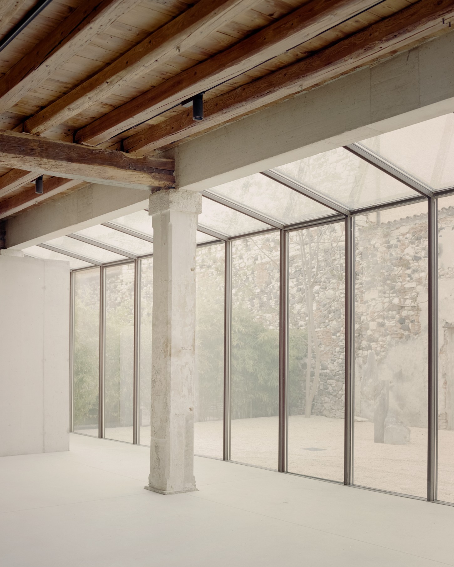 Atipografia Threshold and Treasure Gallery by AMAA — The interior of the Atipografia Threshold gallery reveals a post-and-beam structural system with exposed timber beams overhead and a white concrete column...
